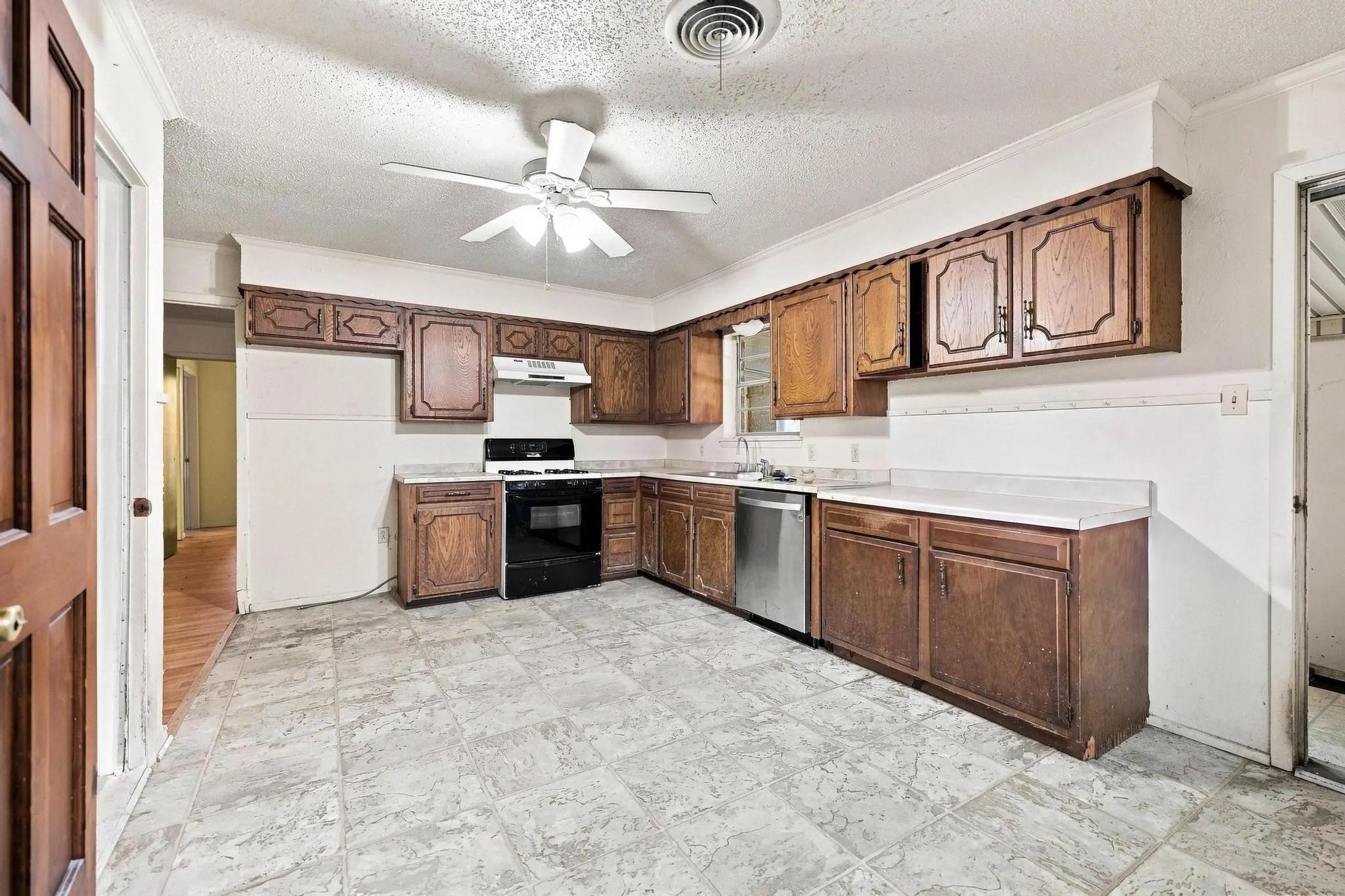 Kitchen featuring wood cabinetry, light countertops, a stainless steel dishwasher, and a black range