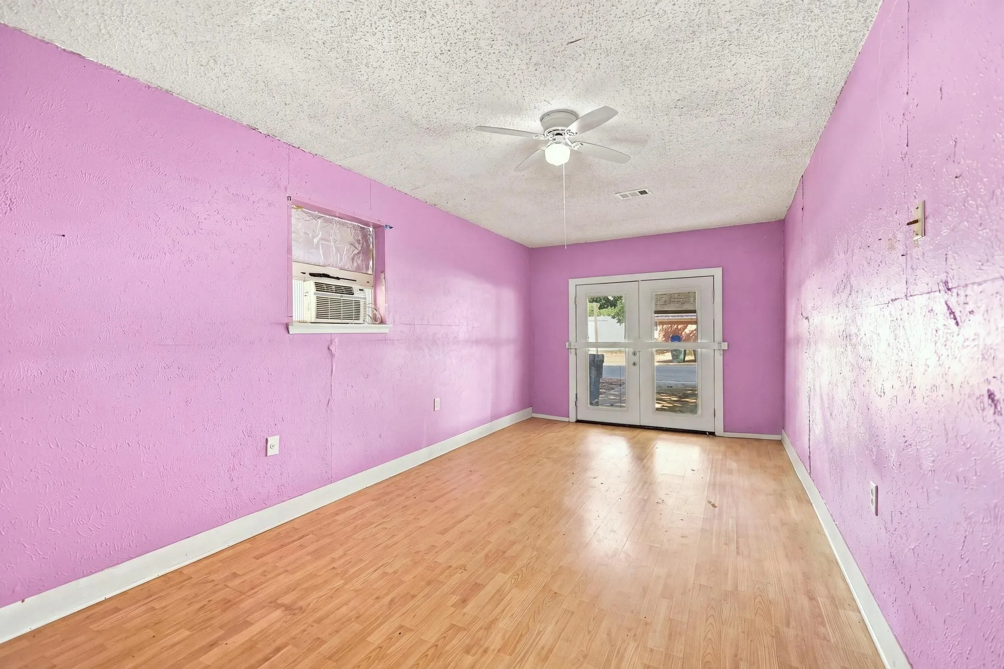 Spacious room with vibrant pink walls, wood-finish flooring, and abundant natural light from a window