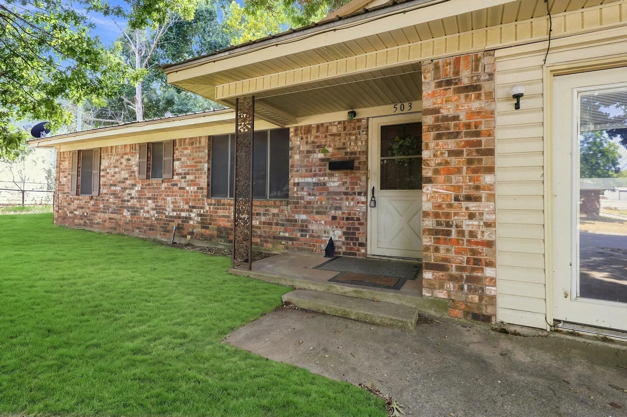 Brick facade with contrasting siding sections, covered entry, front door with a decorative screen door, and multiple windows with screens