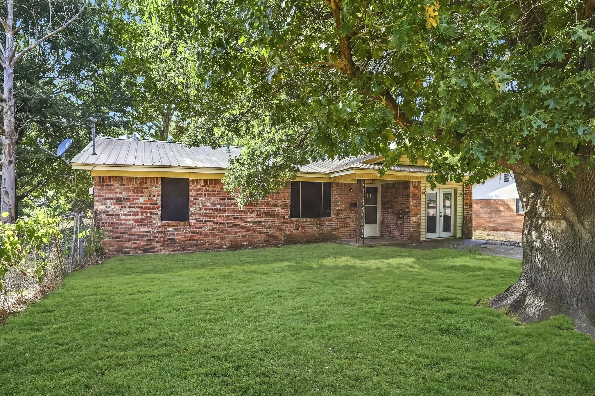 Brick exterior with a metal roof, covered porch, and mature trees