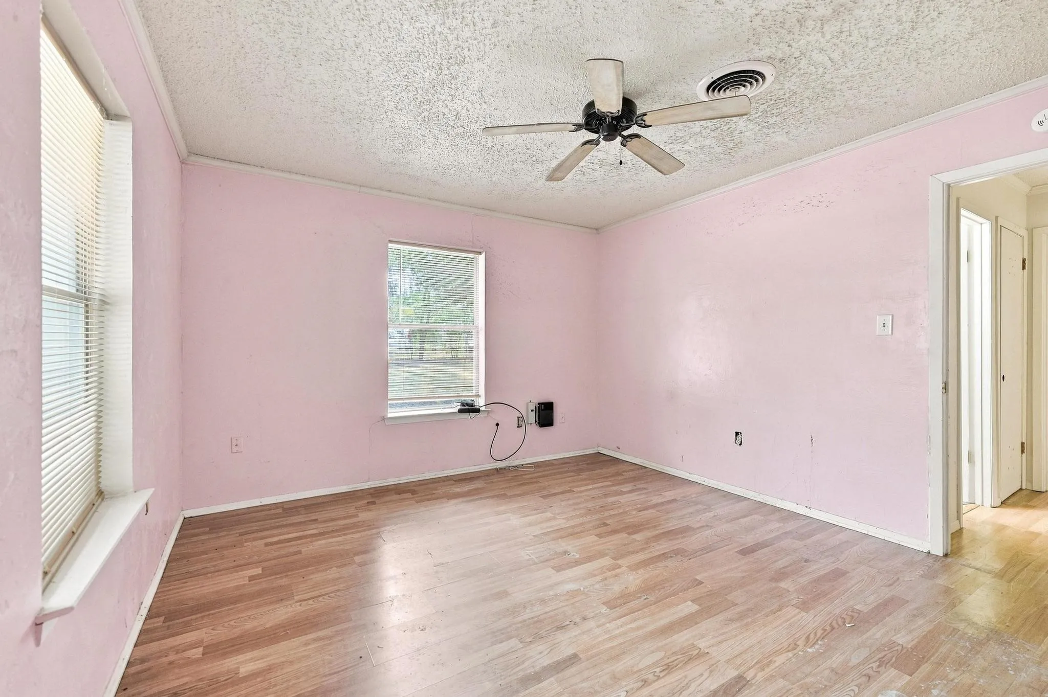Room with wood-finish flooring, two windows with blinds, and a ceiling fan