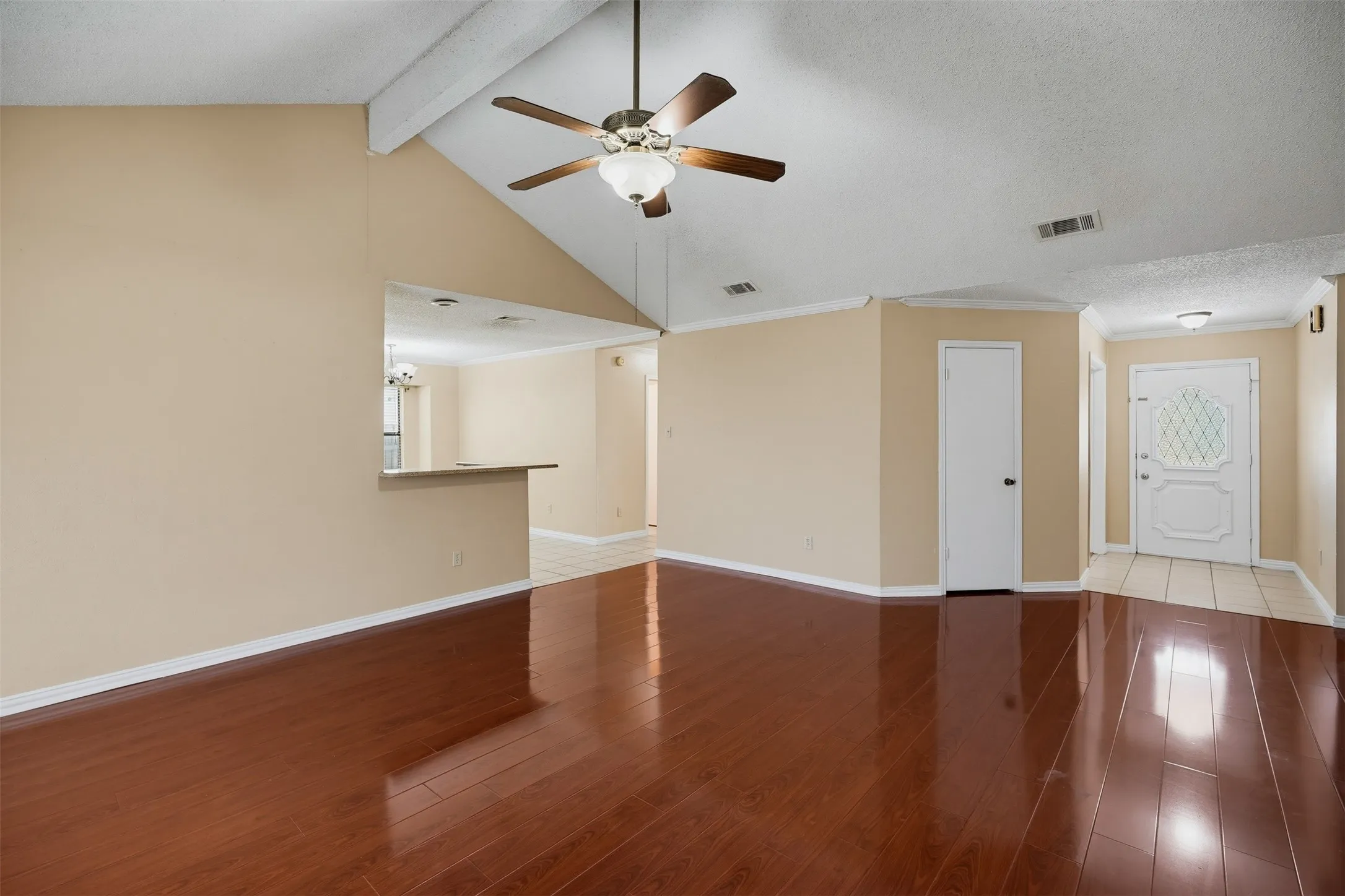Vaulted ceiling with a ceiling fan, wood-finish flooring, interior pass-through window, and a white paneled entry door with decorative glass