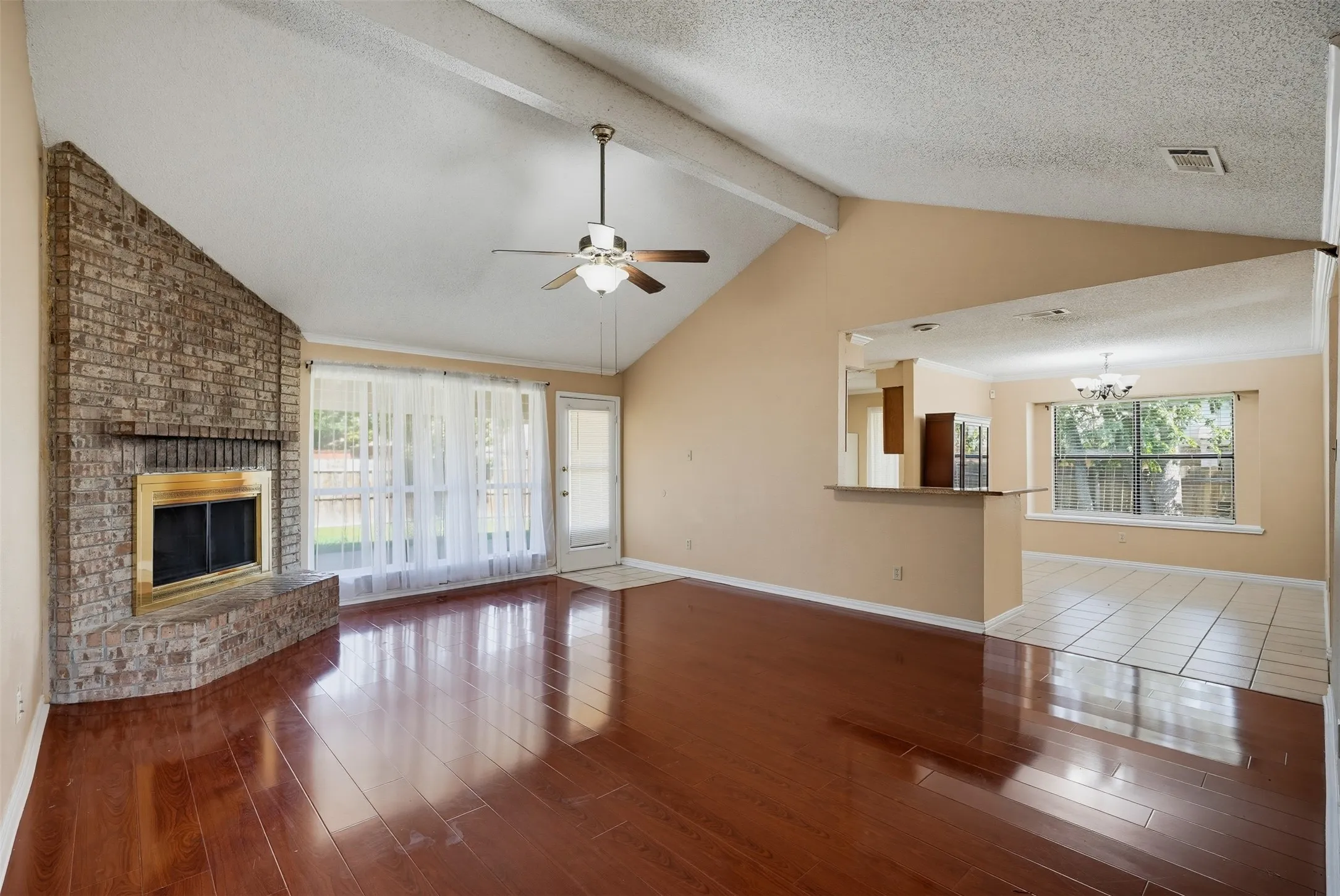 Vaulted ceiling with exposed beams, brick fireplace, wood-finish flooring, and a pass-through bar