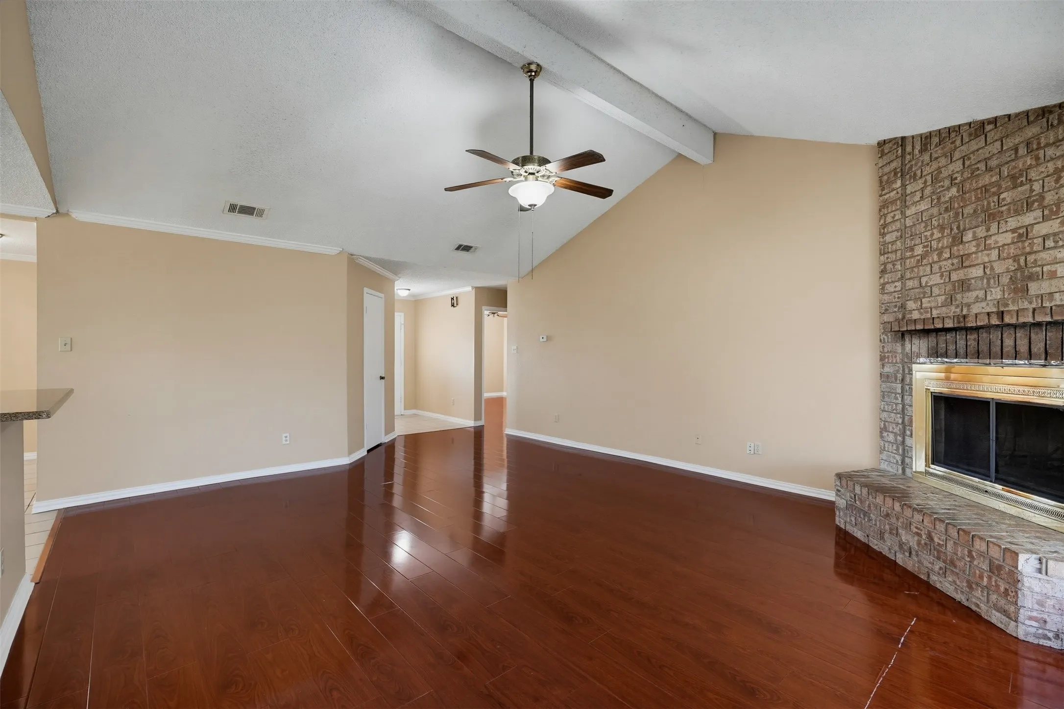 Vaulted ceiling featuring exposed beams, wood-finish flooring, and a brick fireplace with a hearth