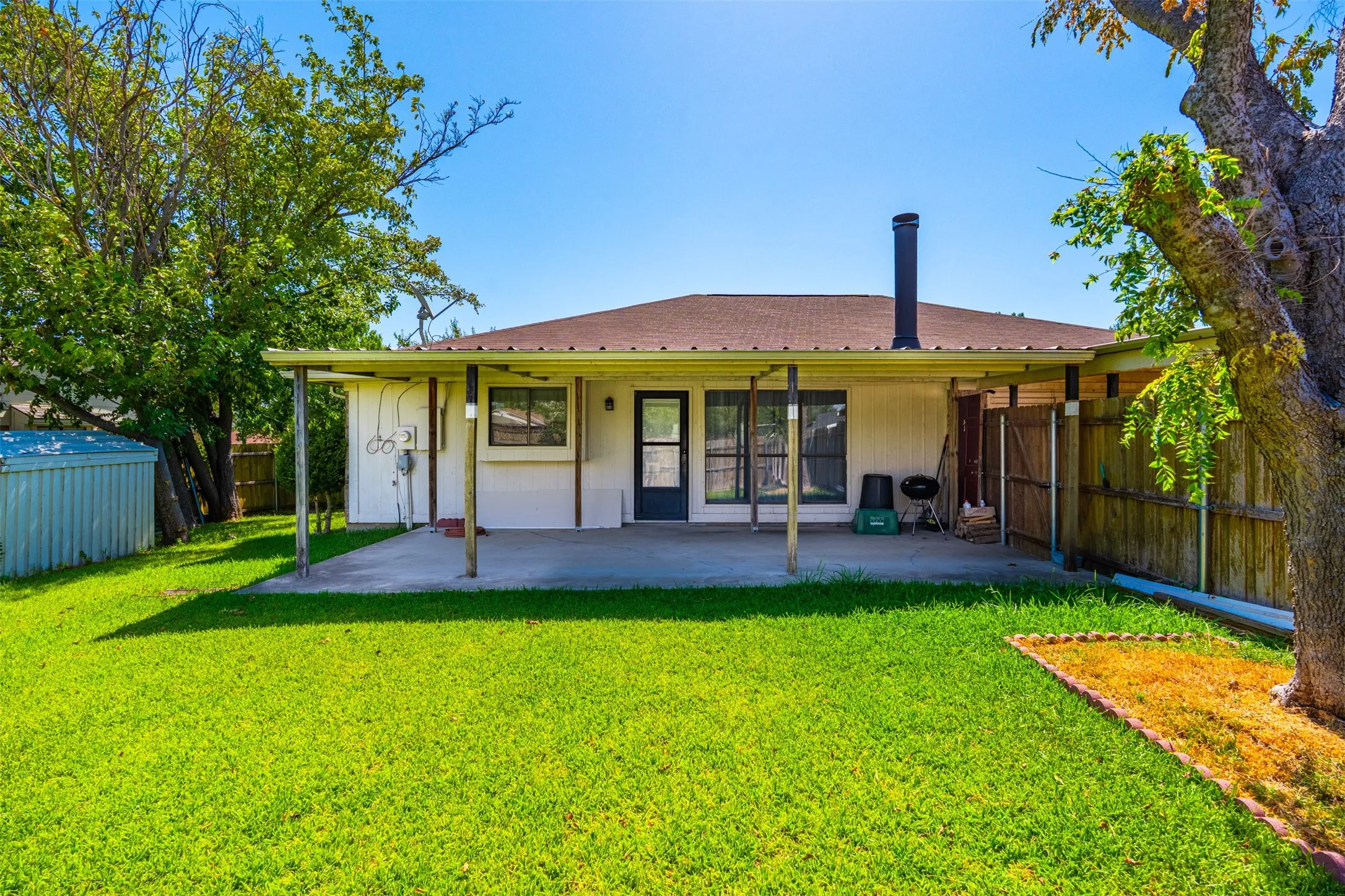 Expansive backyard featuring a covered patio, manicured lawn, and mature trees
