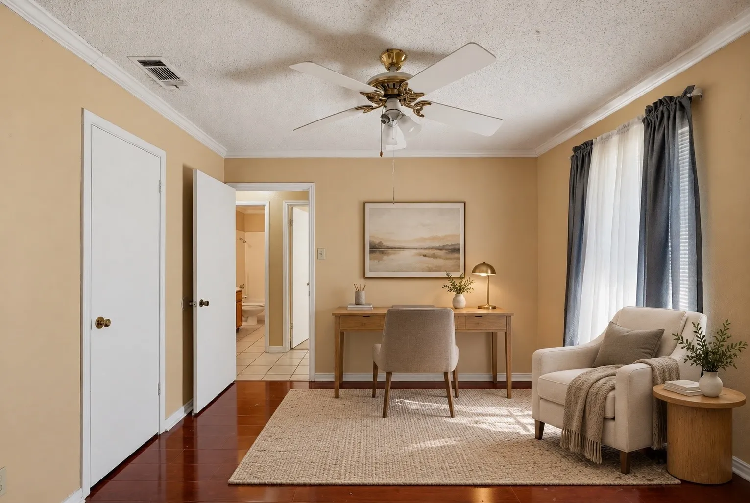 Warm, sun-filled bedroom featuring hardwood flooring, a ceiling fan with brass fixtures, and multiple windows dressed in coordinating drapery