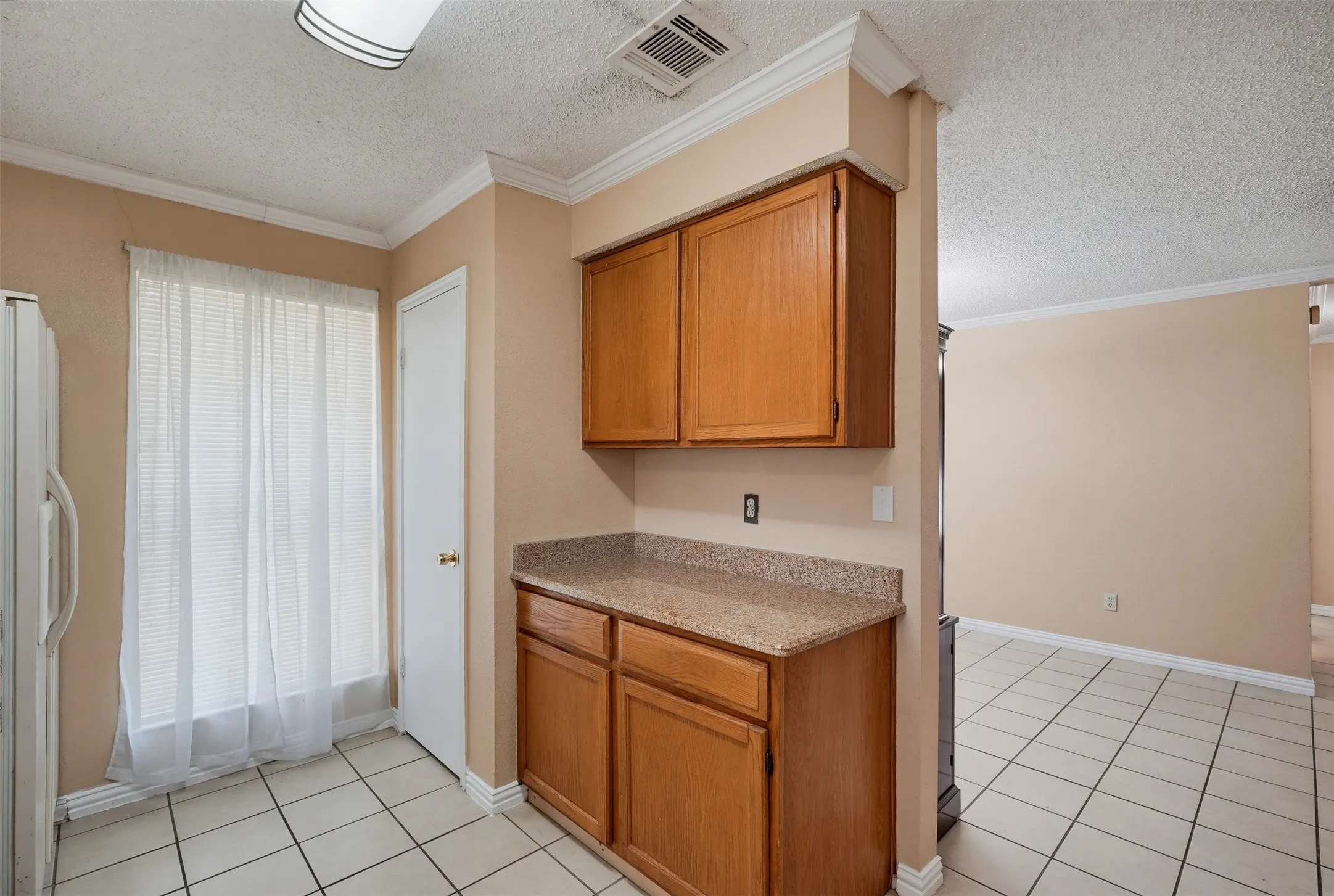 Kitchen featuring wood-finish cabinetry, granite-style countertops, and tile flooring