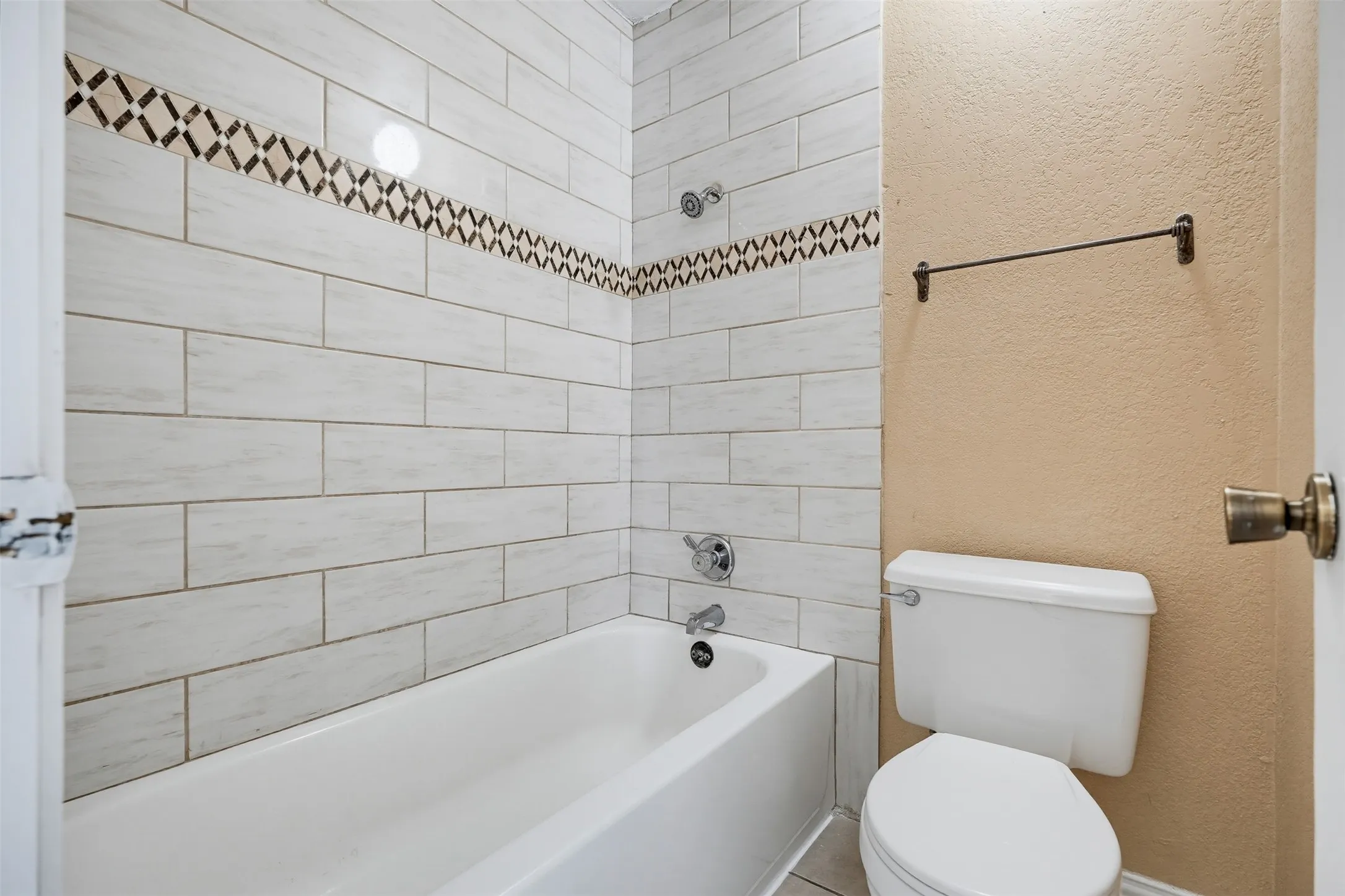 Bathtub with white subway tile surround, decorative accent tile band, and chrome fixtures