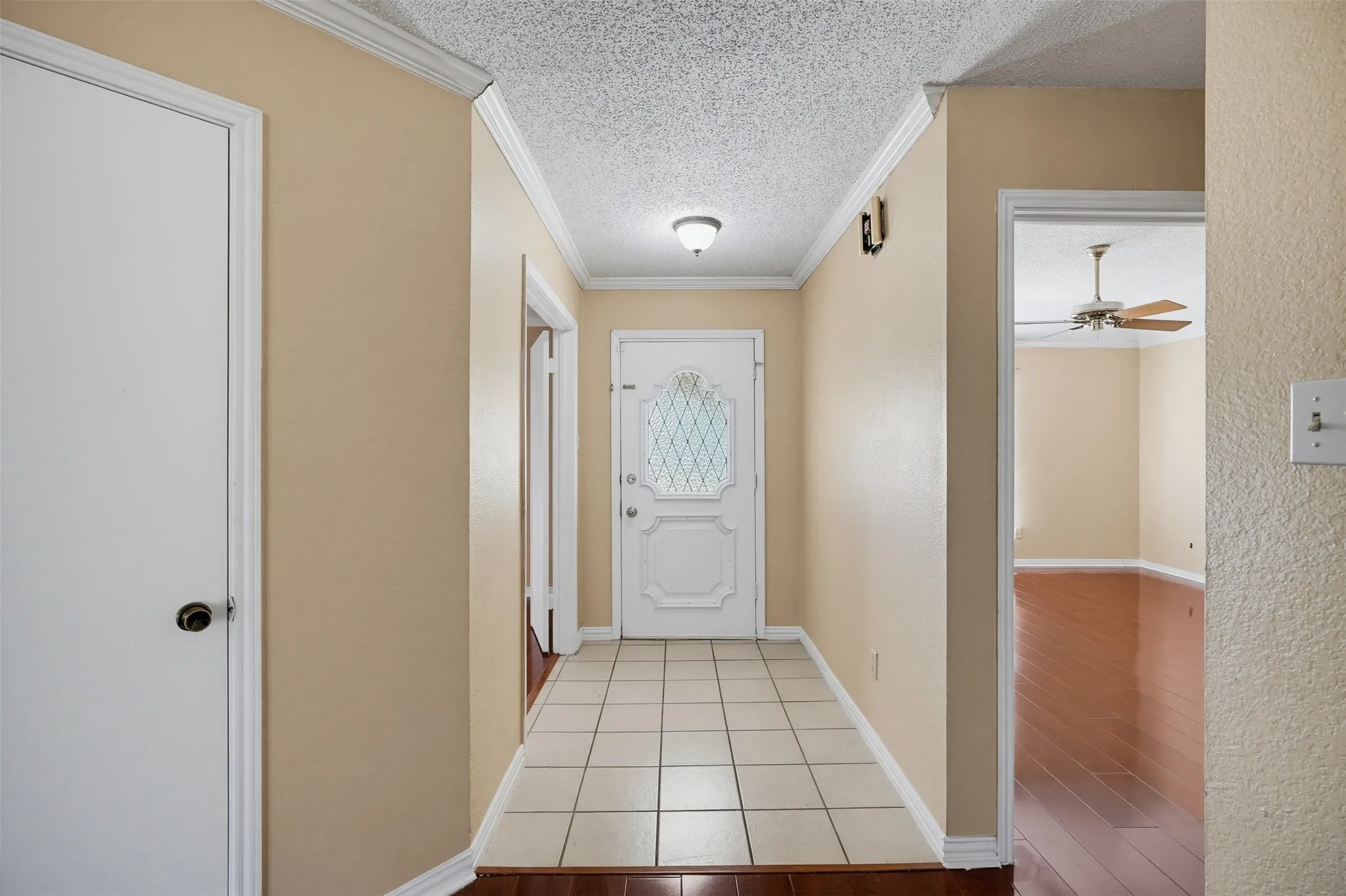 Entryway featuring a white paneled door with decorative glass, cream-colored wall paint, crown molding, and a combination of square tile flooring and wood-finish flooring