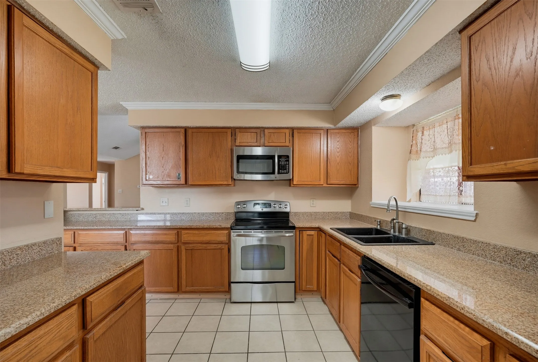 Kitchen featuring wood cabinetry, light-toned countertops, a stainless steel oven, a stainless steel microwave, and tile flooring