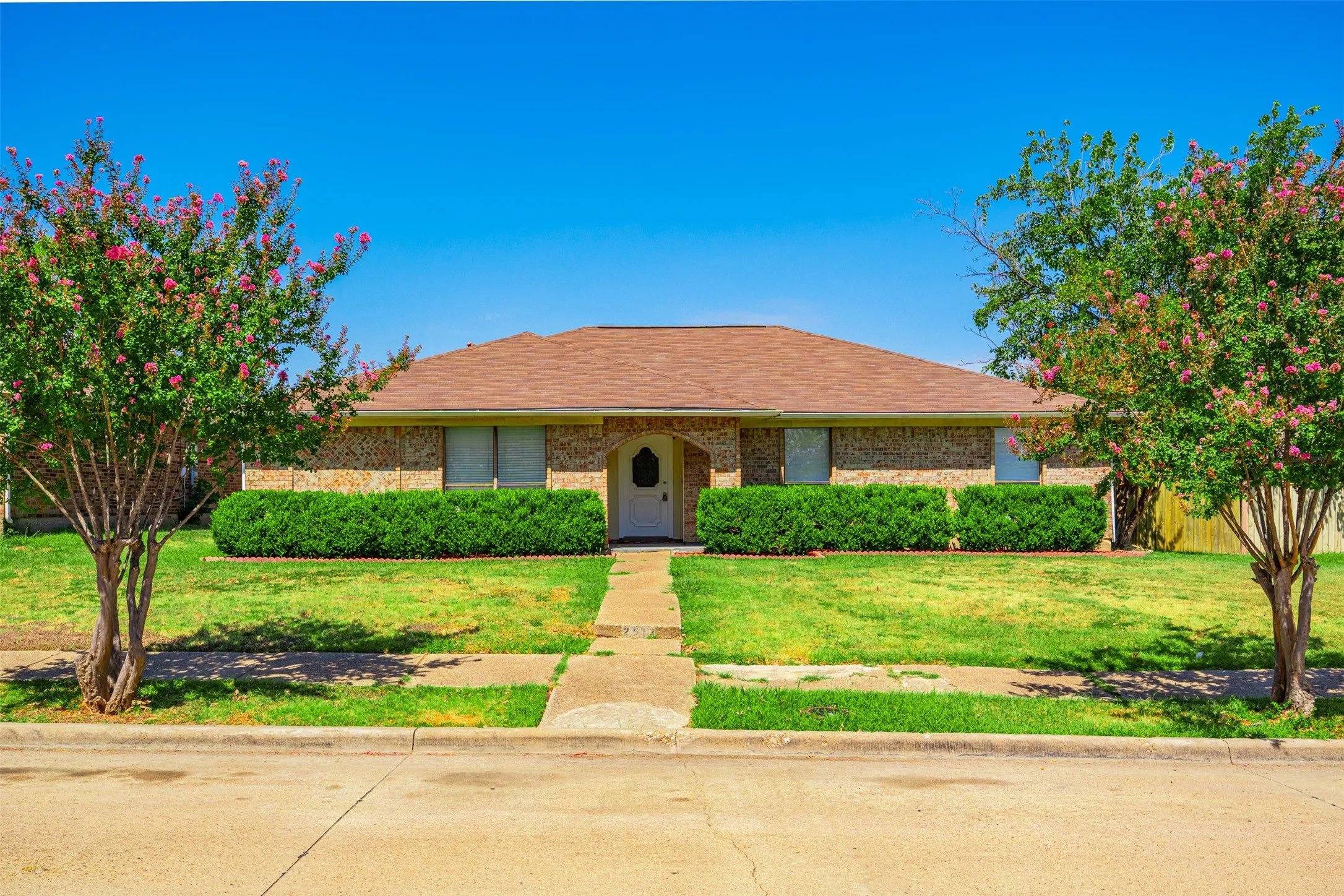 Brick exterior with a brown shingle roof, a white front door, and a concrete walkway