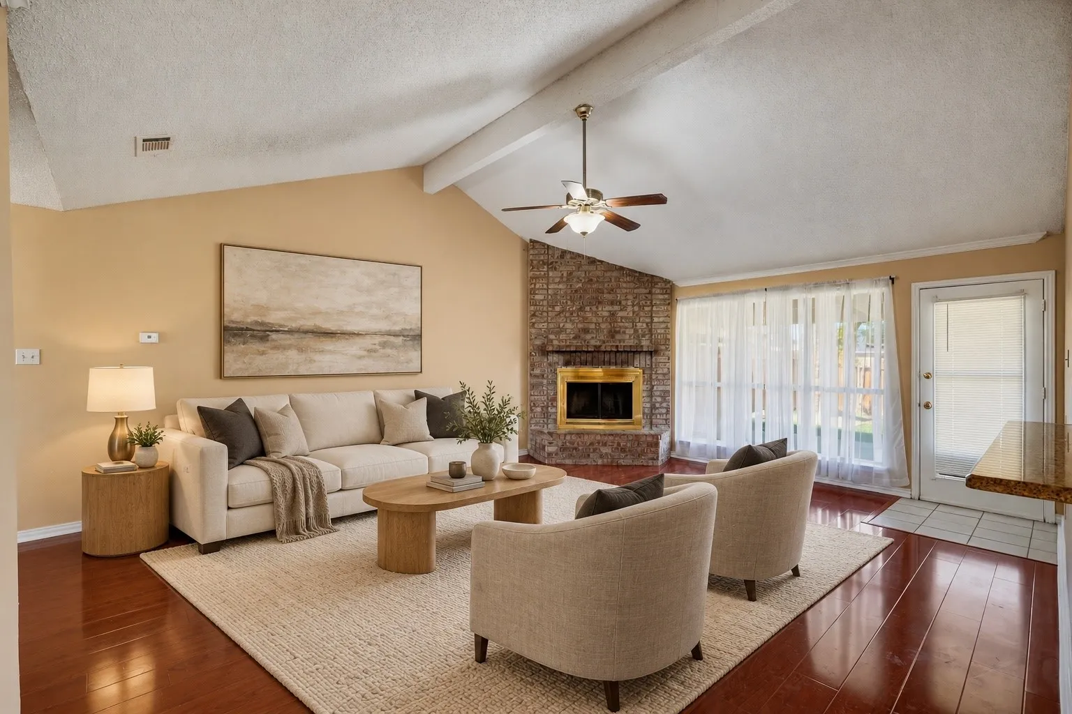 Vaulted ceilings with exposed beams, rich wood-finish flooring, brick-clad fireplace, and an exterior access door with transom window