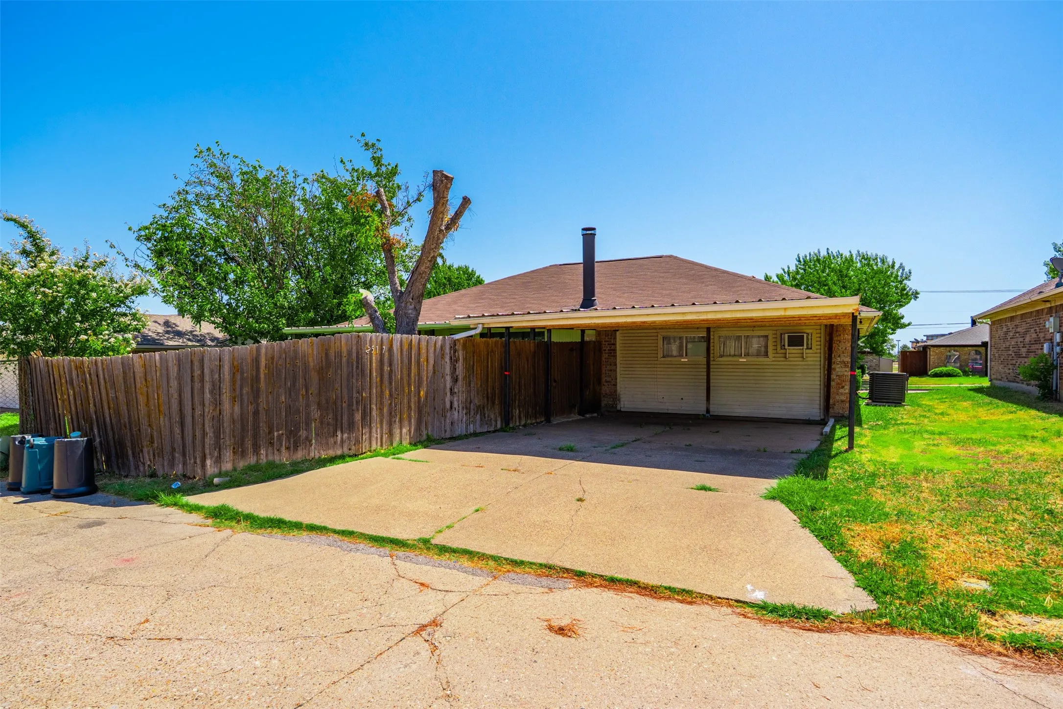 Covered carport, durable wood fence, established trees, and expansive grassy area