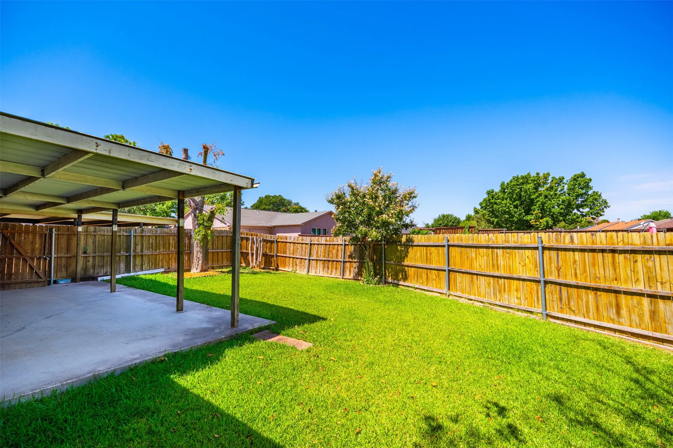 Expansive backyard featuring a covered patio, manicured lawn, and wooden privacy fencing