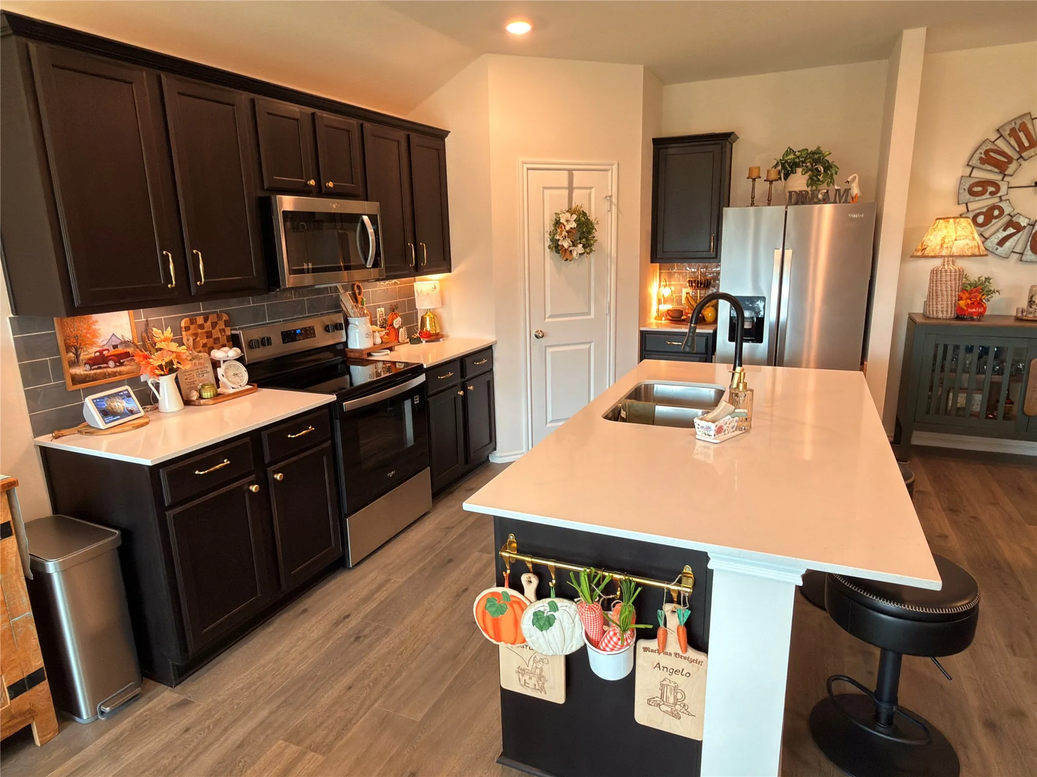 Kitchen featuring dark cabinetry, light countertops, wood-finish flooring, a stainless steel sink with a black faucet, and stainless steel appliances