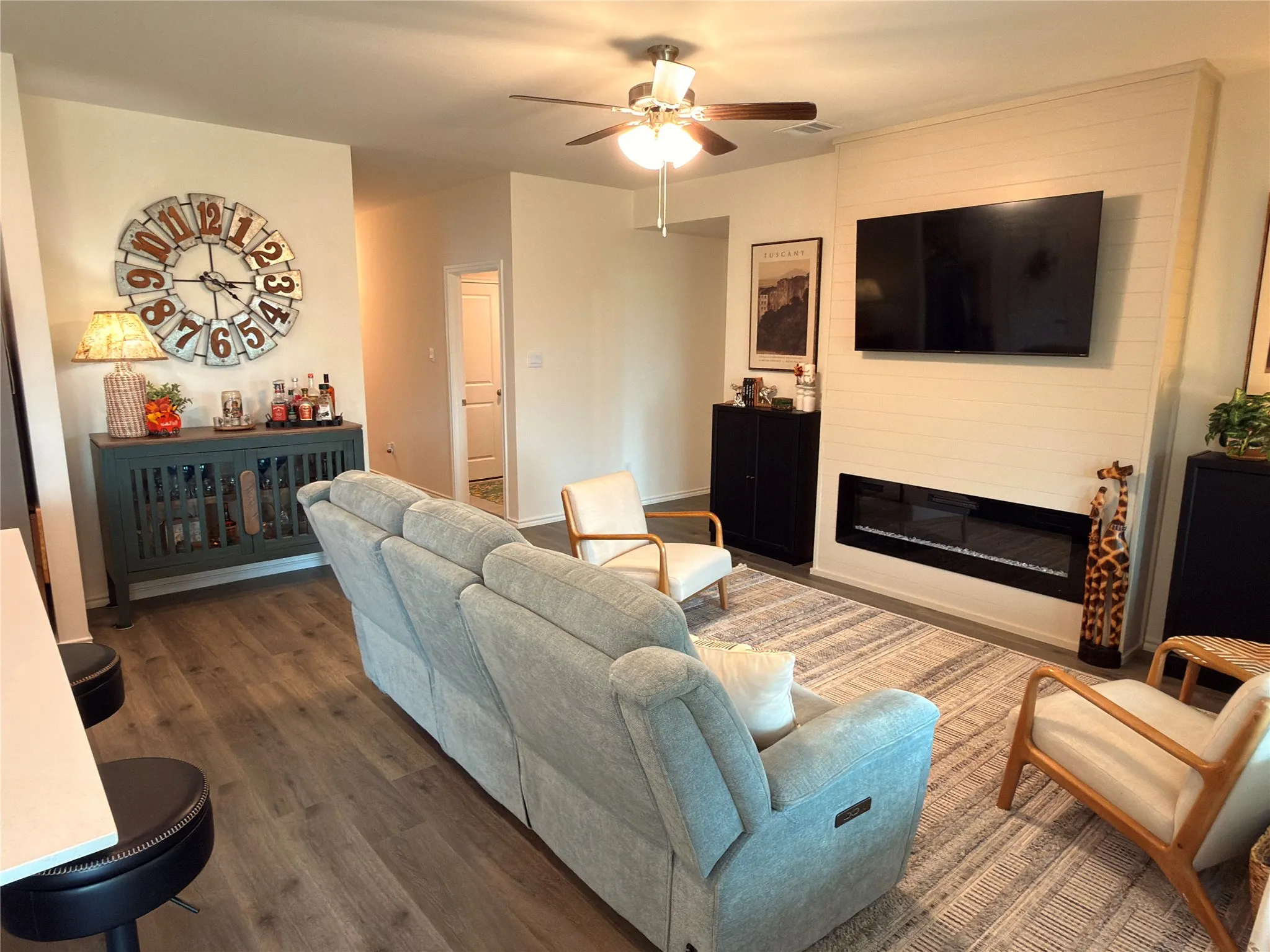 Wood-finish flooring, ceiling fan, shiplap-style accent wall, and built-in electric fireplace