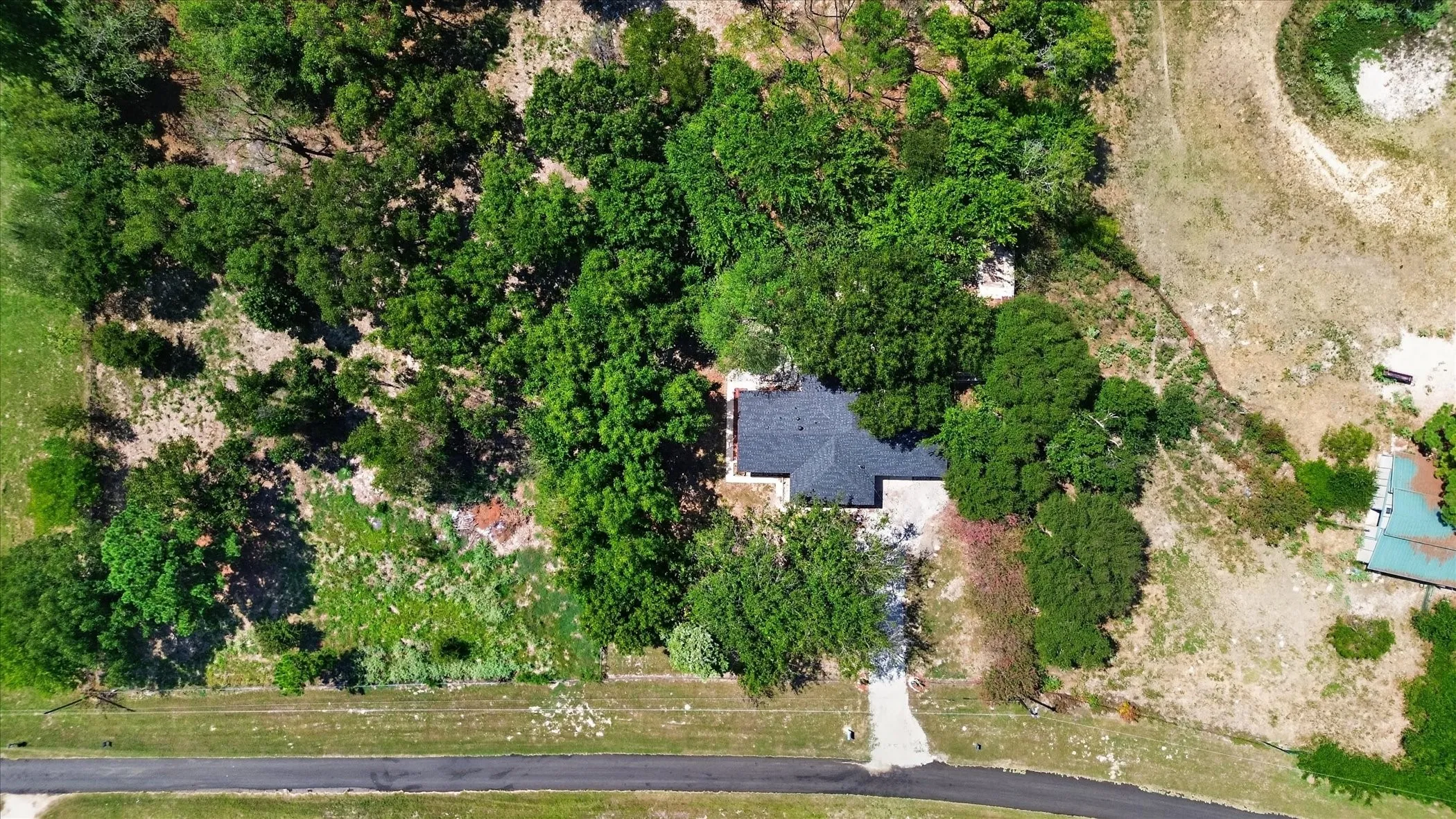 Property featuring a dark shingle roof, mature trees, and a concrete driveway