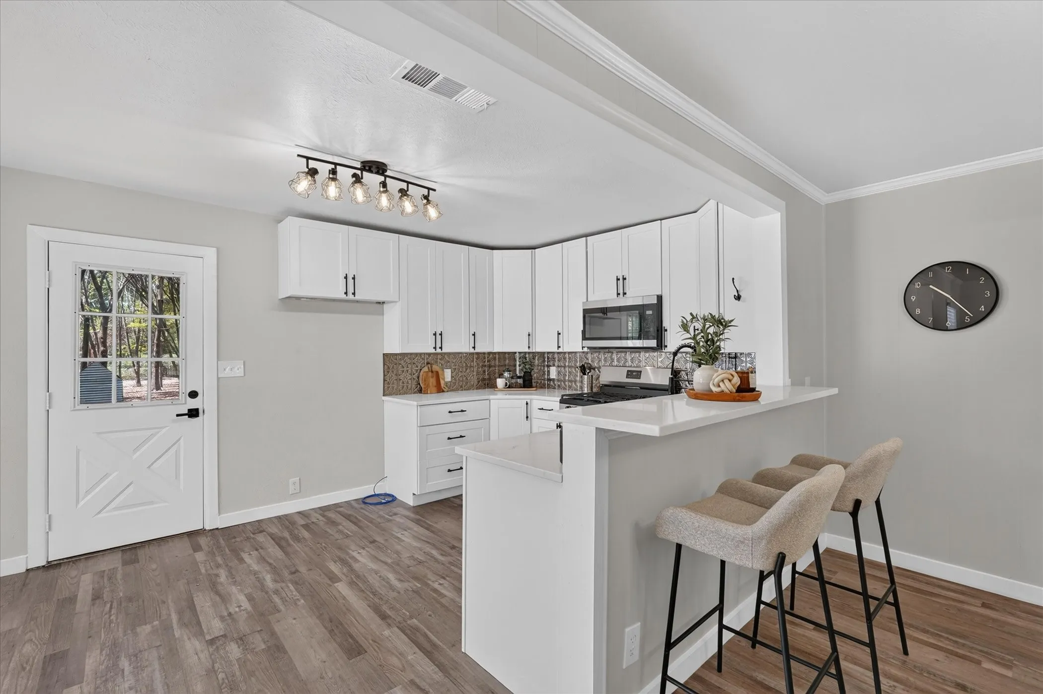 Modern kitchen with white cabinetry and dark hardware, quartz countertops, a tile backsplash, and wood-finish flooring