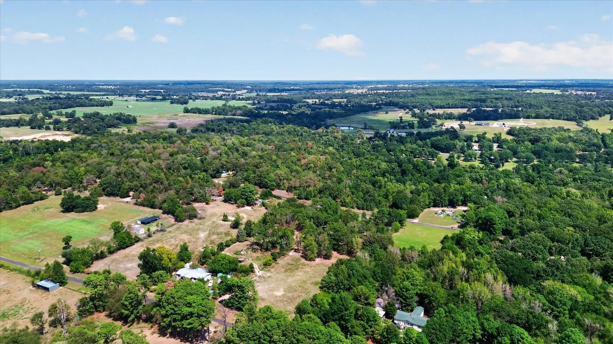 Expansive property featuring dense tree coverage, open clearings, and multiple structures