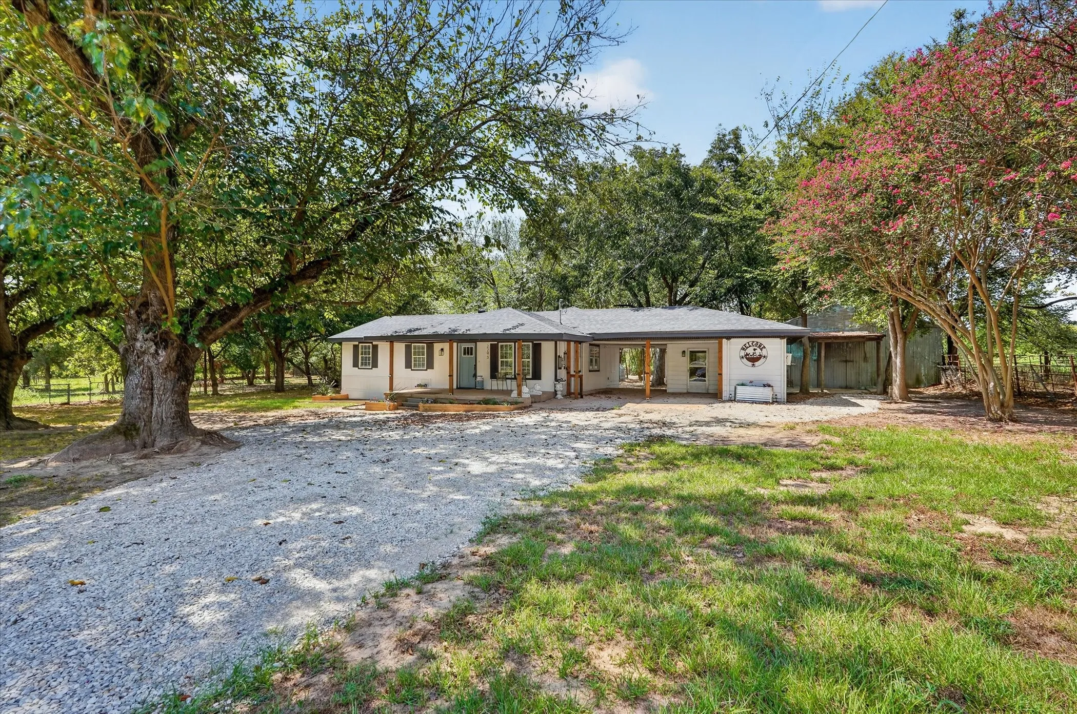 White brick exterior with dark shutters, covered front porch, and a gravel driveway