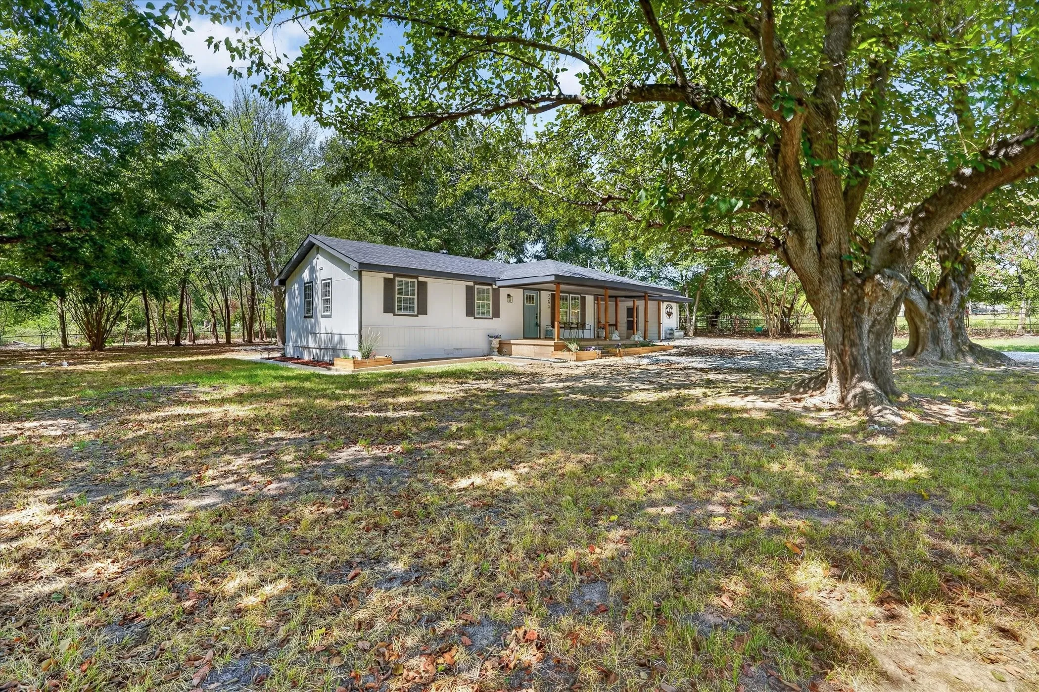 White siding exterior with dark shutters, covered front porch, and mature trees