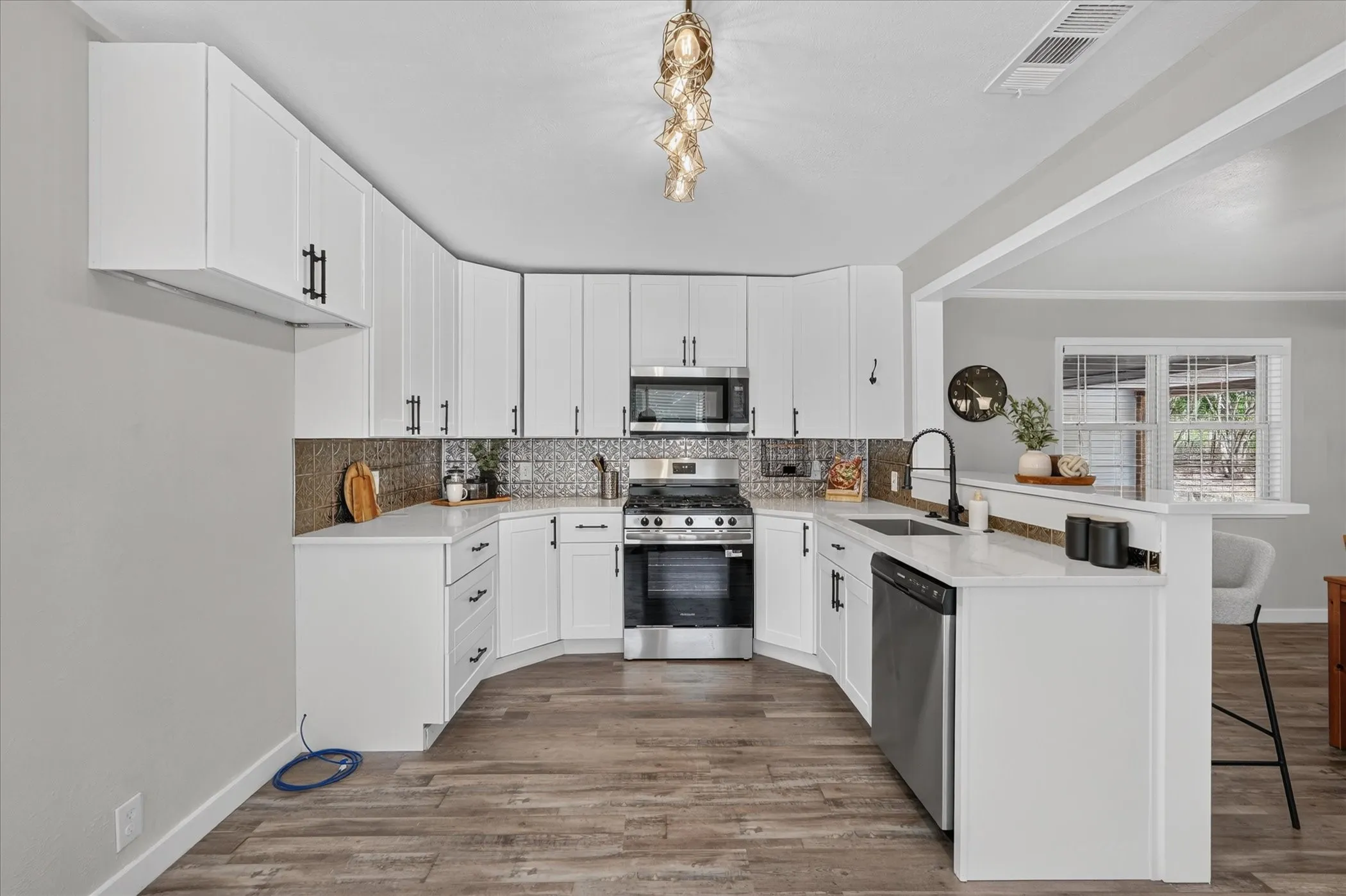 White cabinetry with black hardware, stainless steel appliances, wood-finish flooring, light countertops, and a decorative tile backsplash