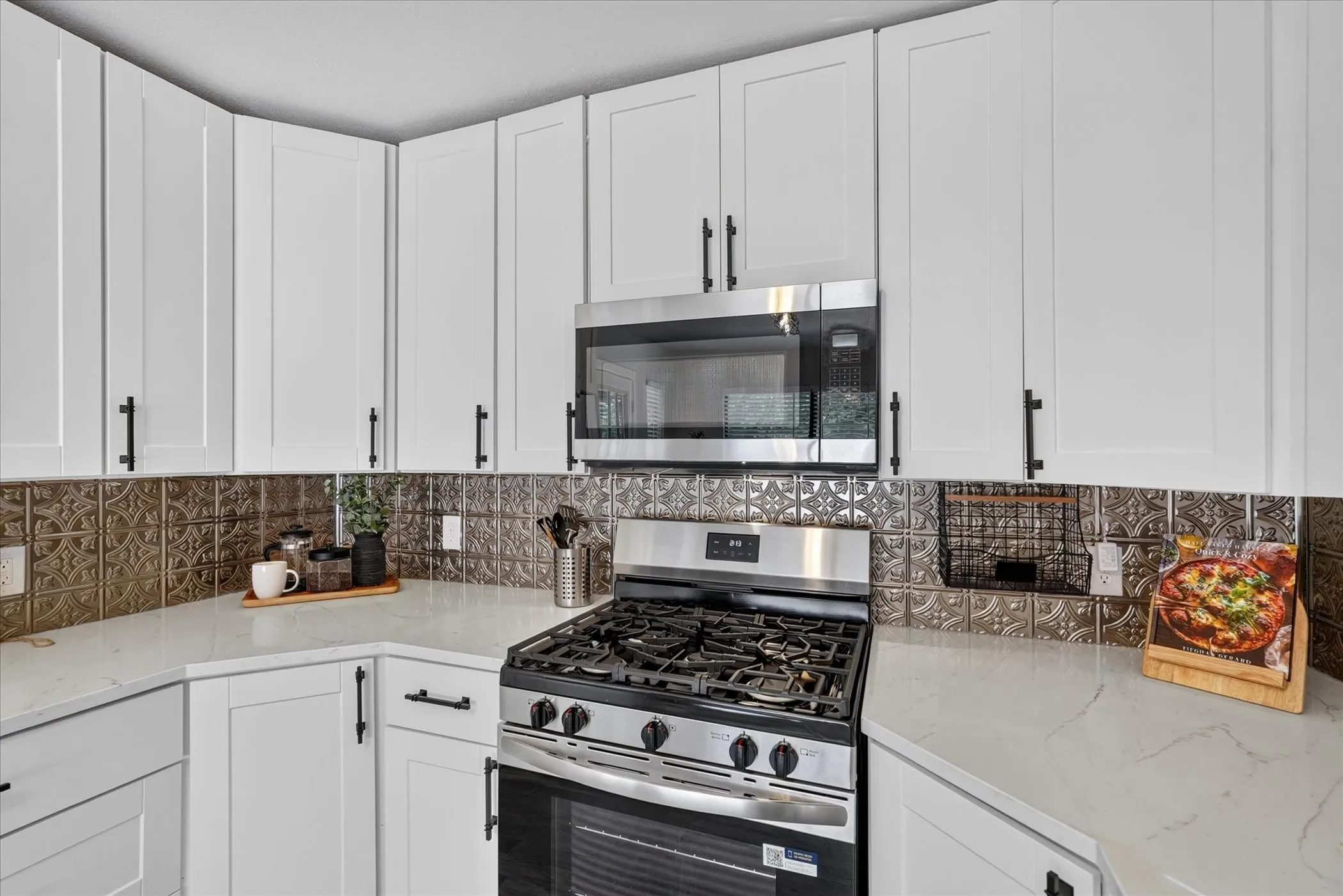 White shaker-style cabinetry, stainless steel oven with gas cooktop, built-in microwave, white countertops, and decorative backsplash