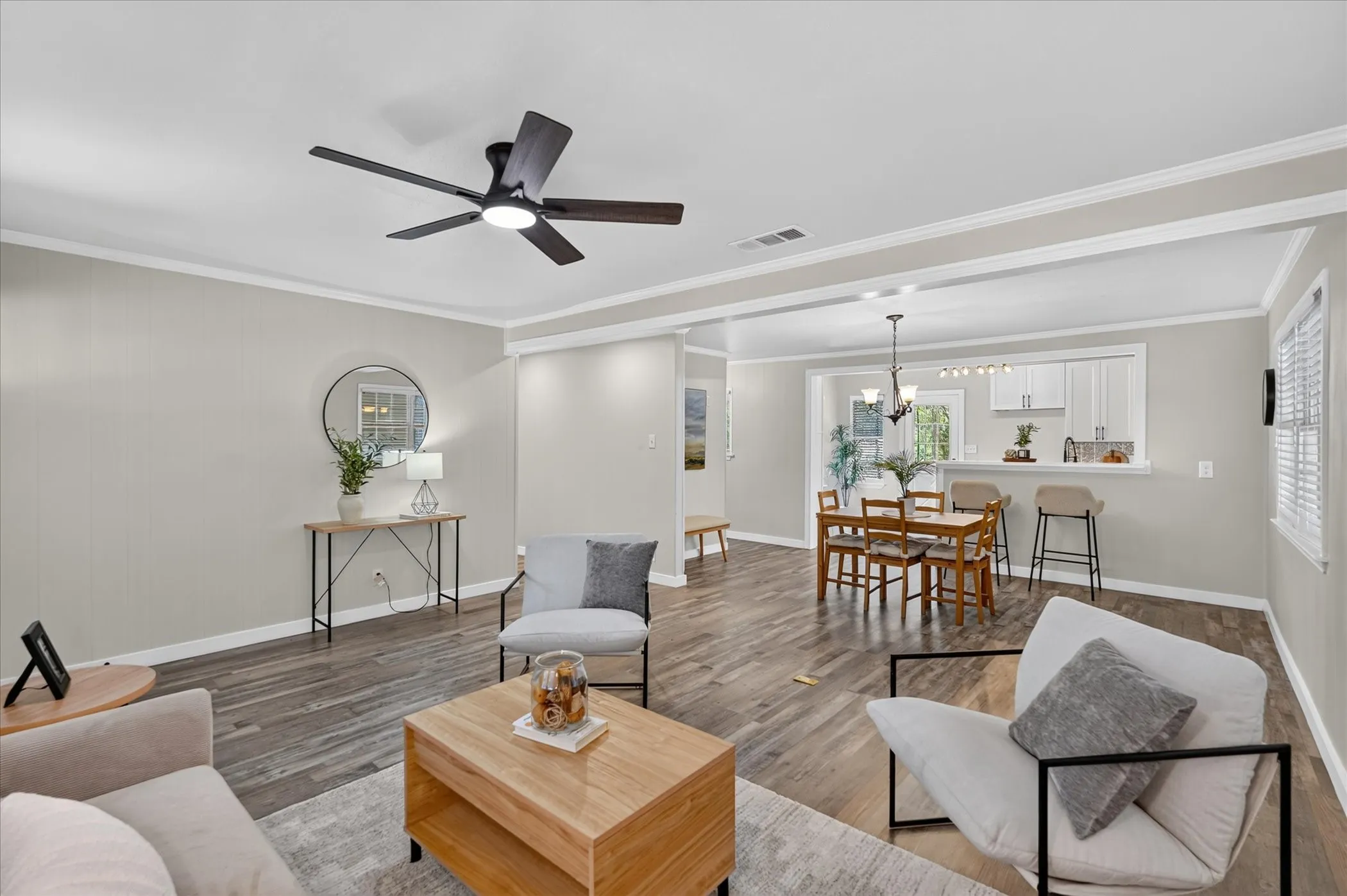 Open-concept living space featuring wood-finish flooring, a modern ceiling fan, and crown molding