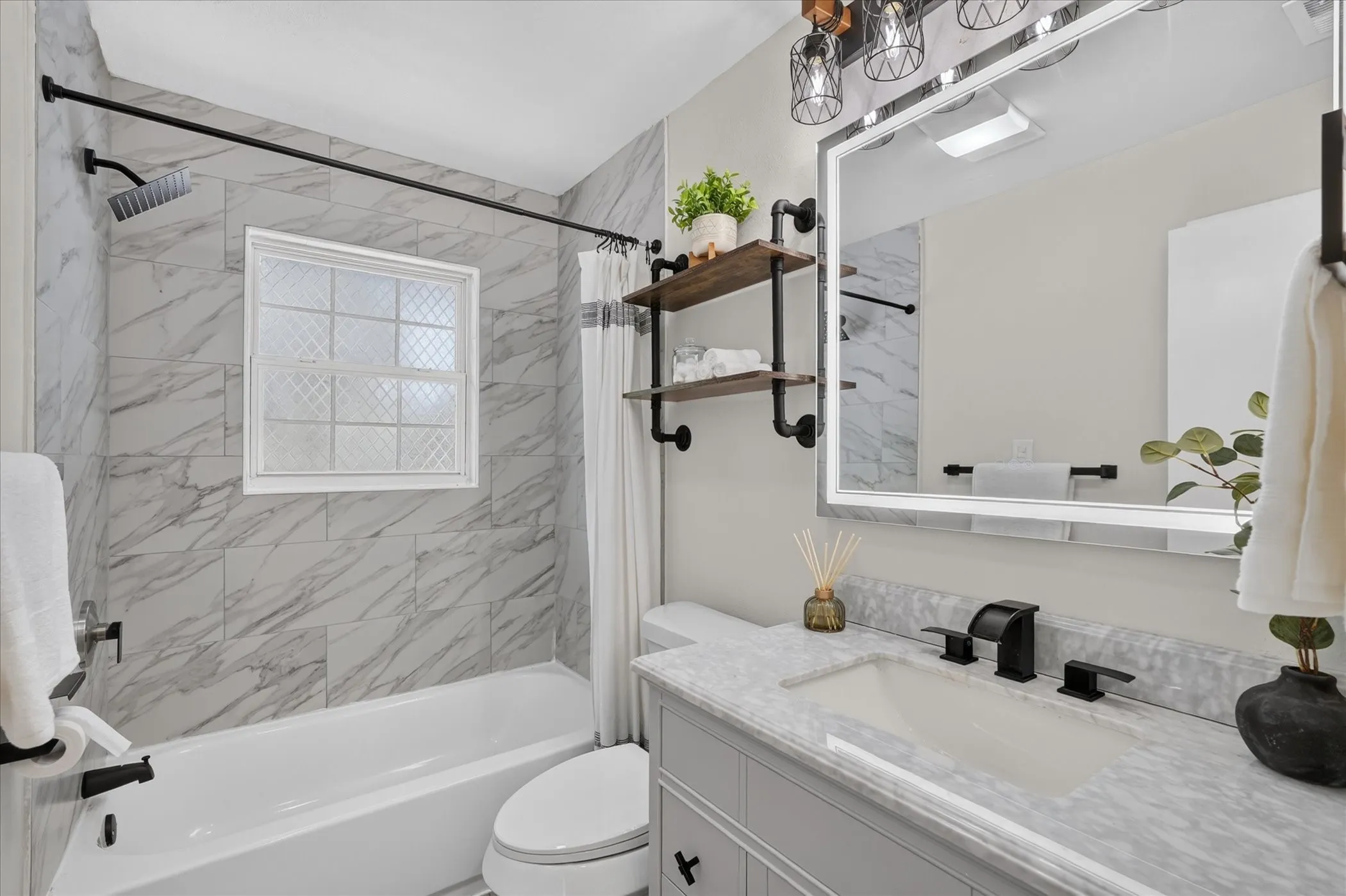 Bathroom featuring a built-in tub with a shower, patterned tile surround, a single vanity with a solid surface countertop, an integrated sink, and an illuminated mirror