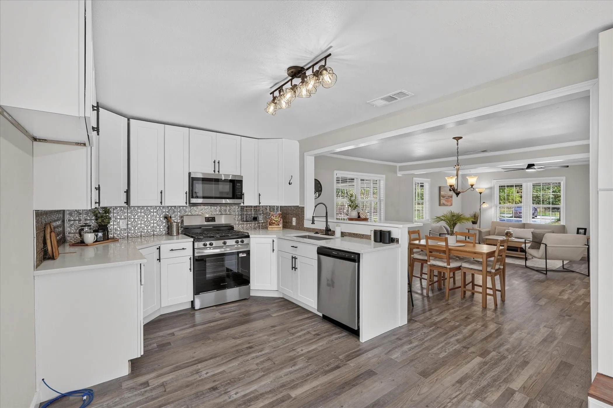 Kitchen featuring white cabinetry, stainless steel appliances, patterned tile backsplash, and wood-finish flooring