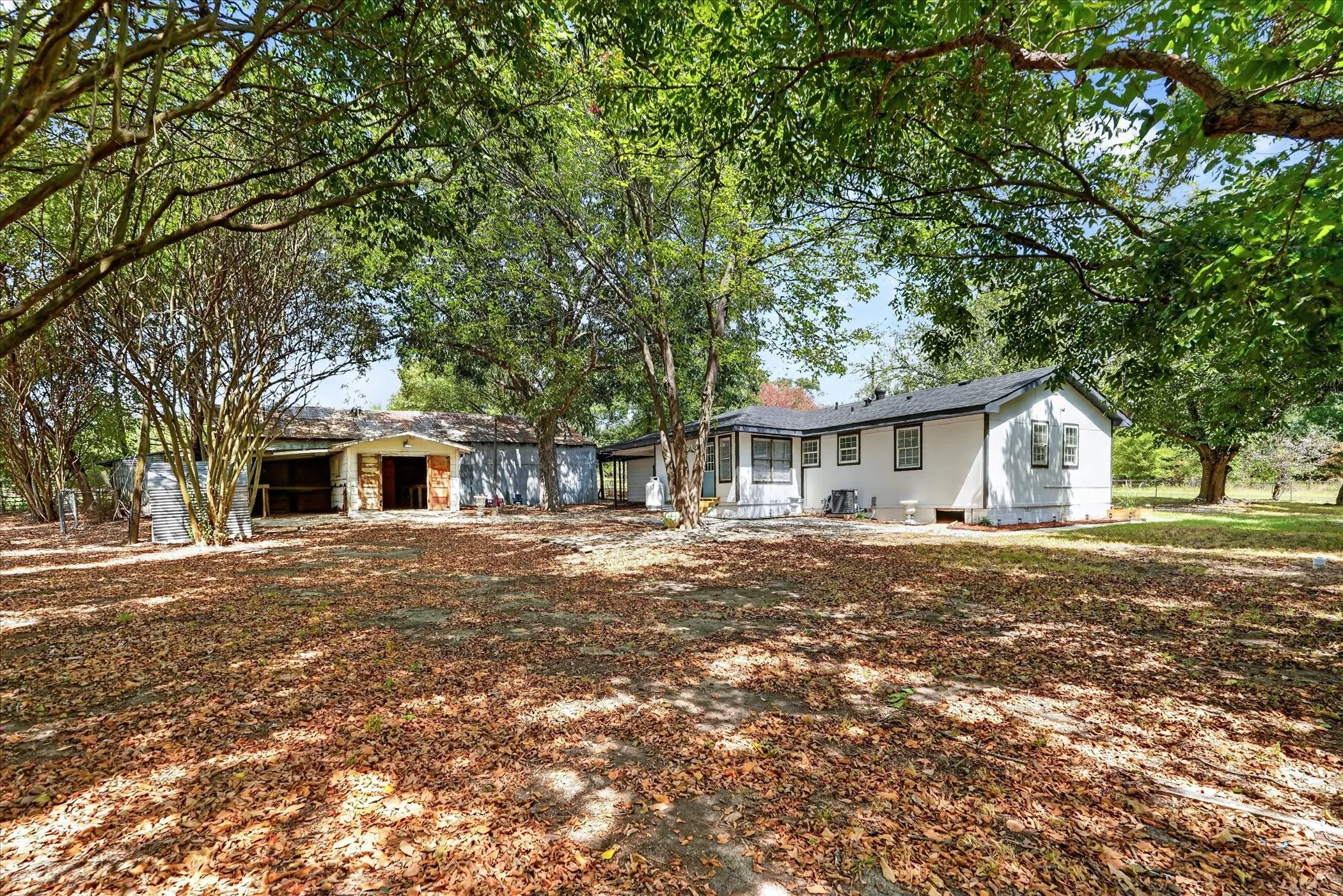Expansive outdoor area featuring mature trees, a white-sided residence with black trim, and a separate utility structure