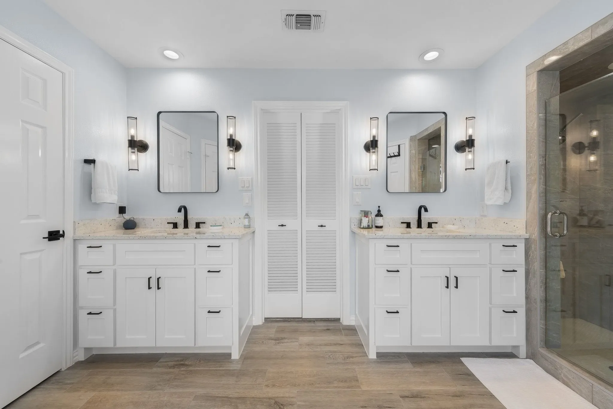 Dual white vanities with speckled countertops, black fixtures, and framed mirrors