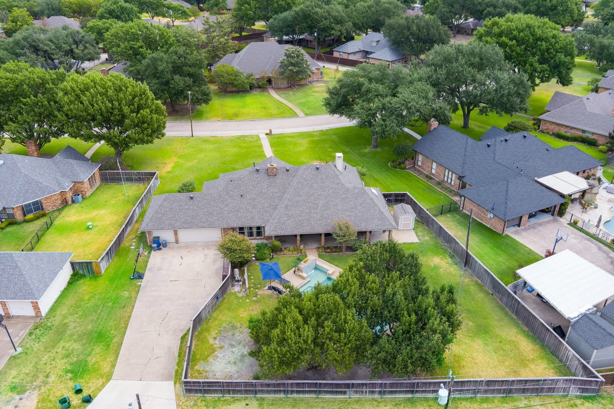 Expansive residential lot featuring a paved driveway, mature trees, and a fenced perimeter