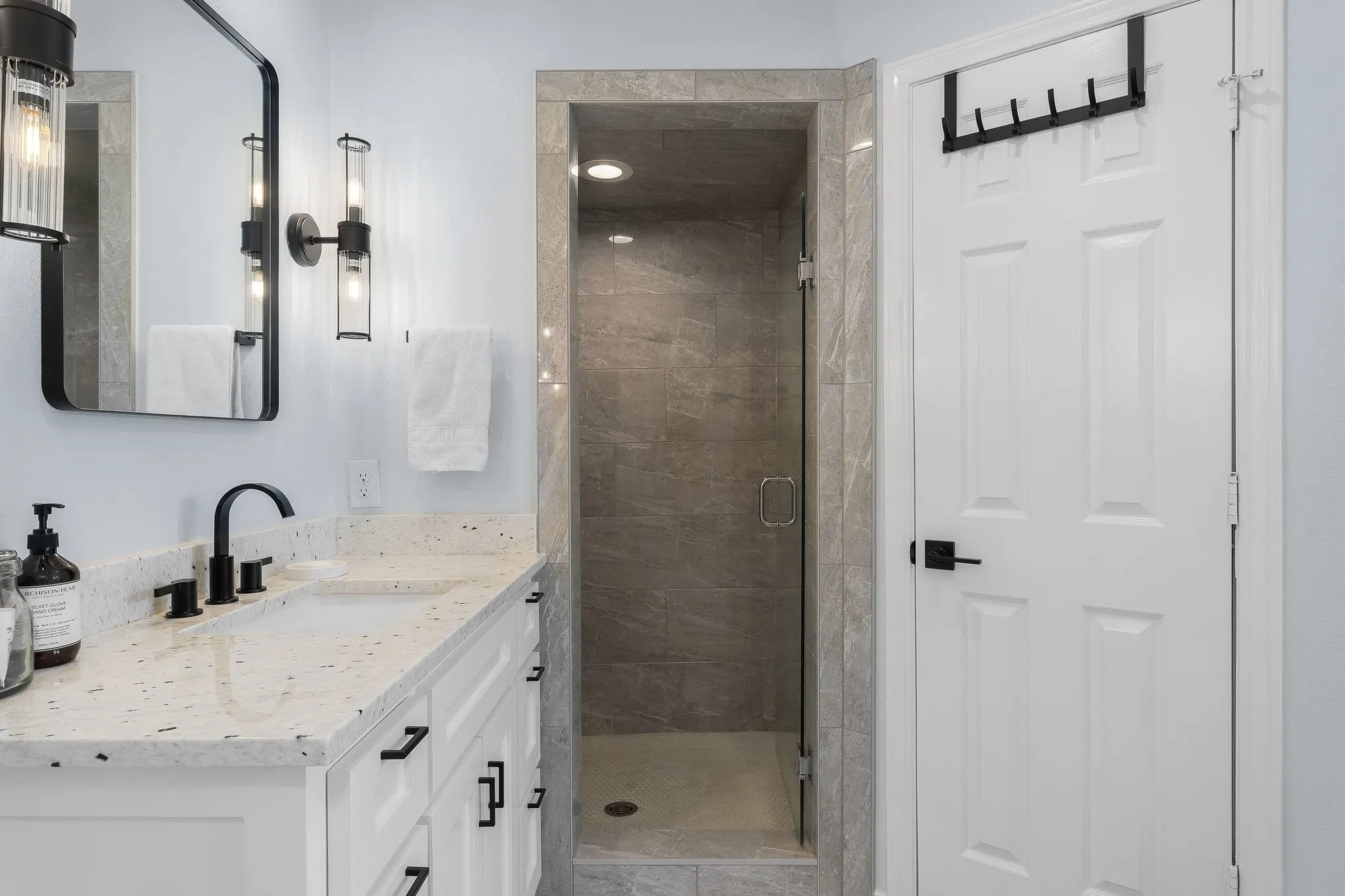 White vanity with a light-colored countertop and integrated sink, matte black faucet, and a frameless glass-enclosed shower with full-height tile surround