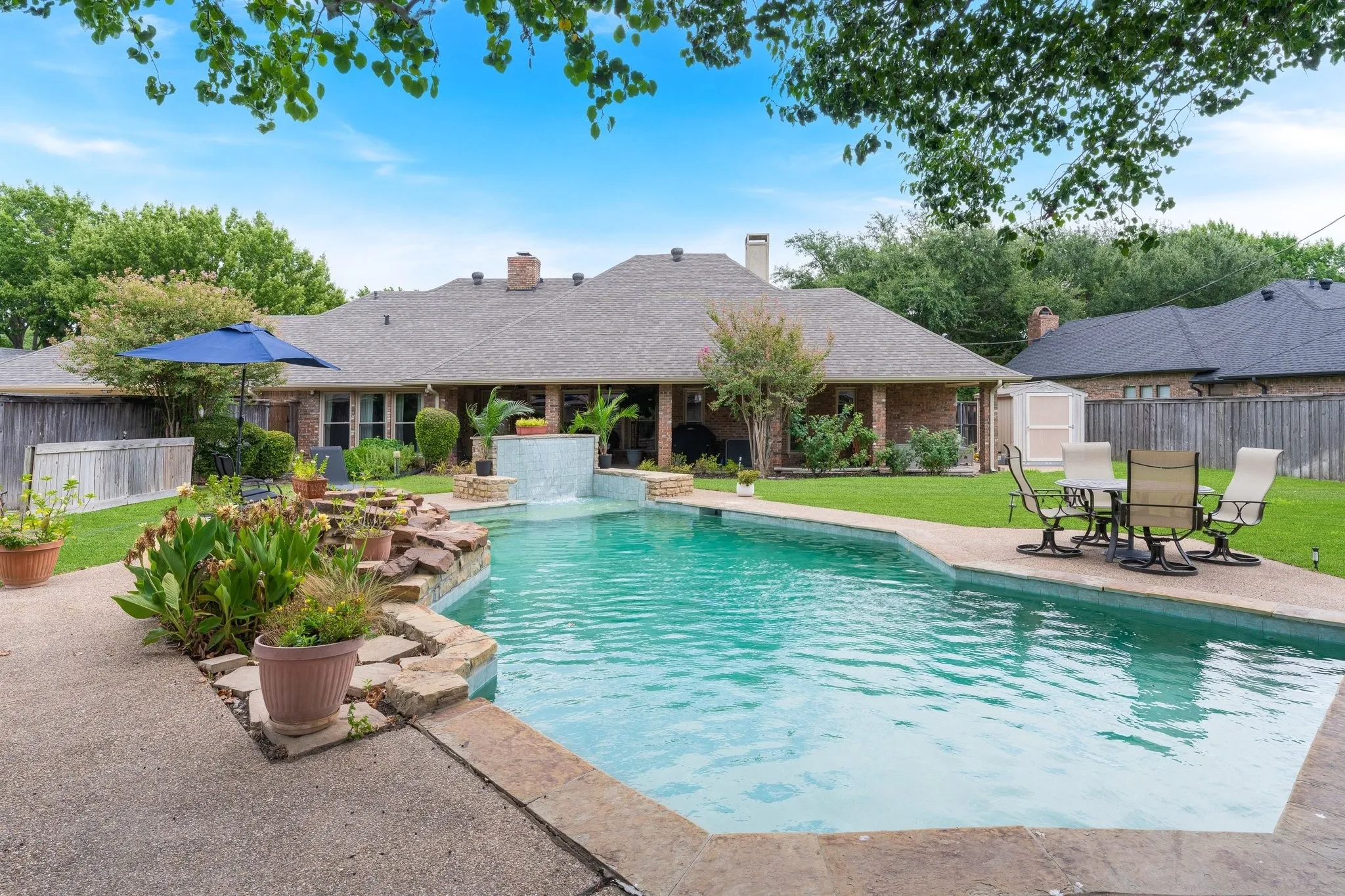 Outdoor swimming pool with integrated waterfall feature, surrounding stone hardscaping, and verdant landscaping