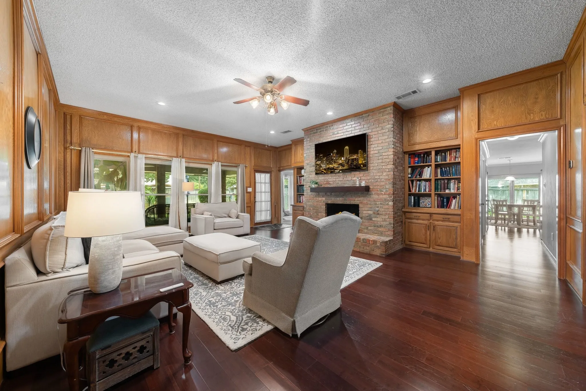 Expansive living room showcasing rich wood-finish flooring, coffered wood ceiling with ceiling fan, and recessed lighting