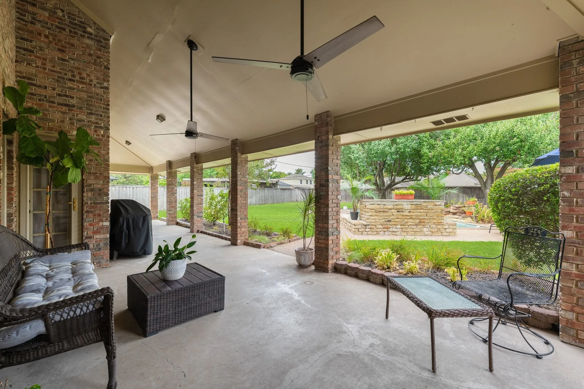 Covered patio with brick columns, dual ceiling fans, and concrete flooring