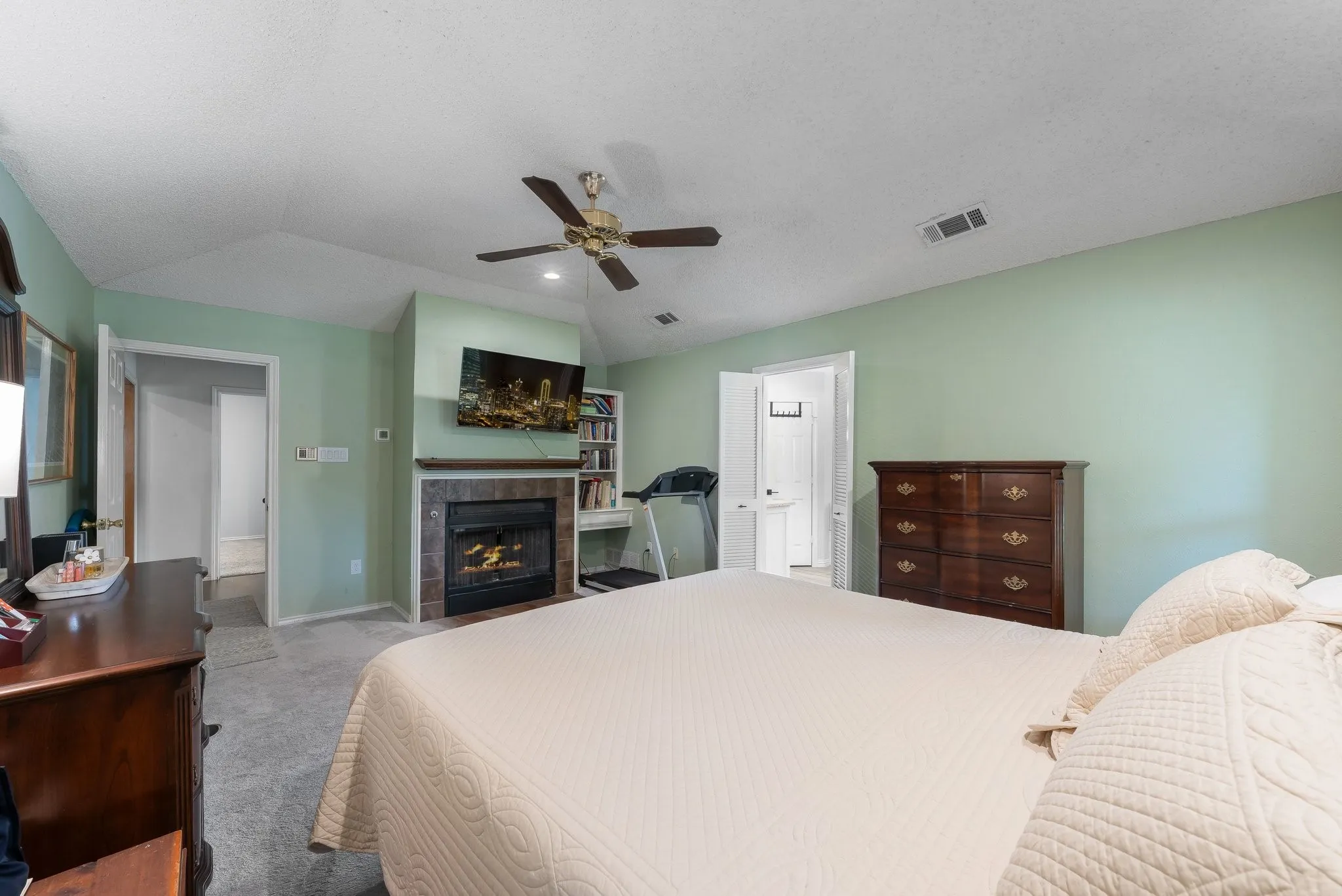 Vaulted ceiling, ceiling fan, fireplace with stone surround, wood-finish mantel, and built-in shelving