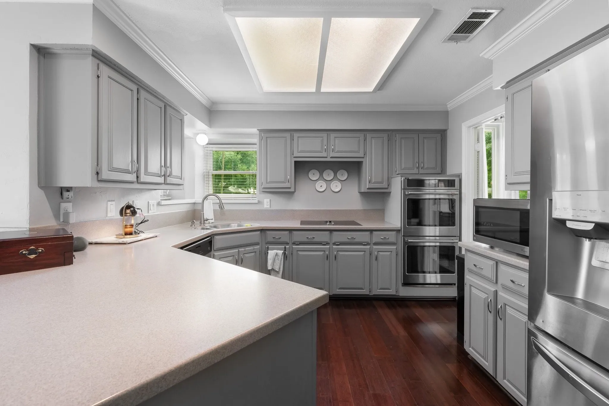 Chef's kitchen featuring custom gray cabinetry with recessed panel doors, stainless steel double wall ovens, and a substantial quartz-topped island with seating