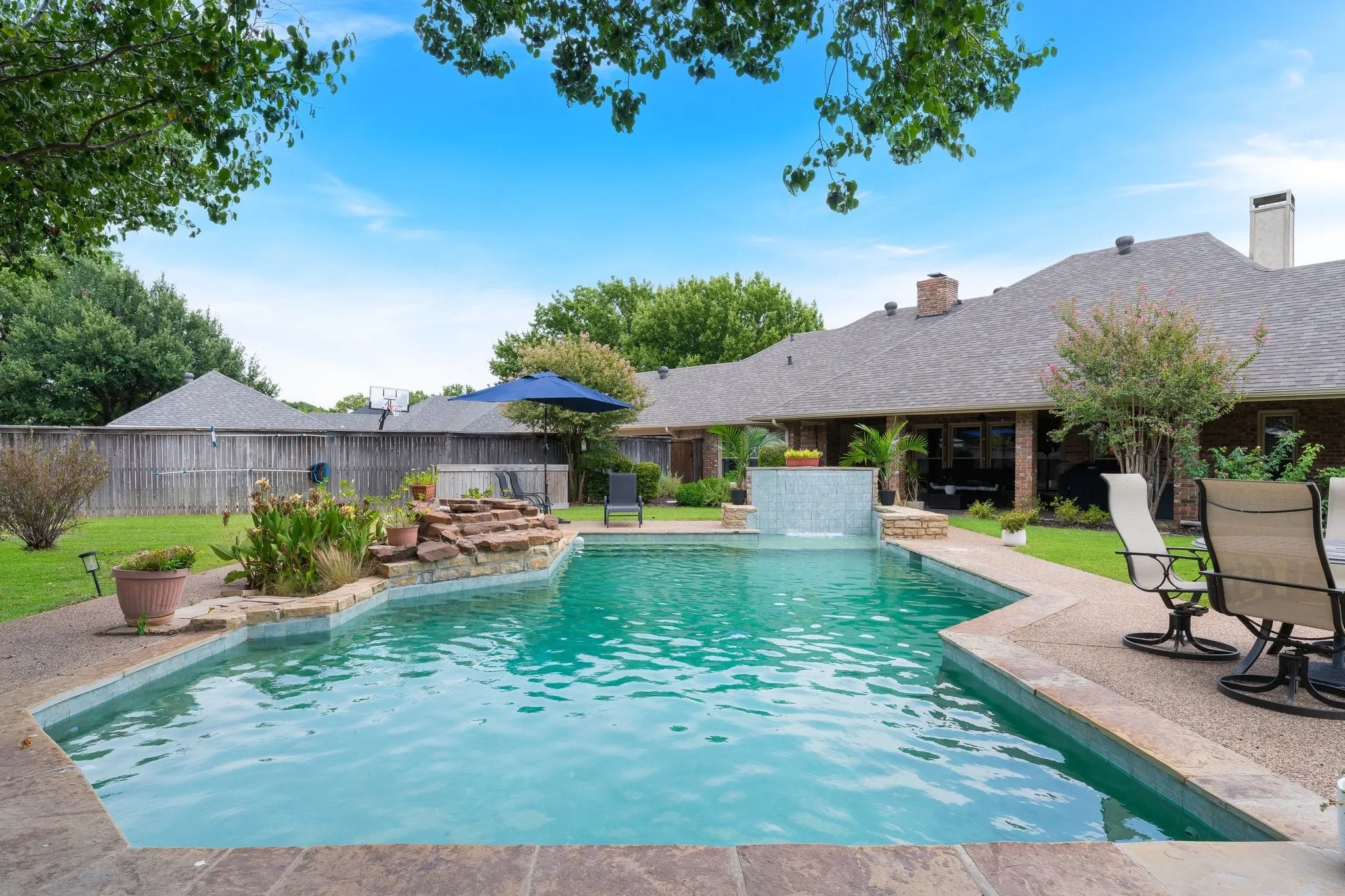 Swimming pool with integrated waterfall feature, stone coping, and adjacent hardscaping