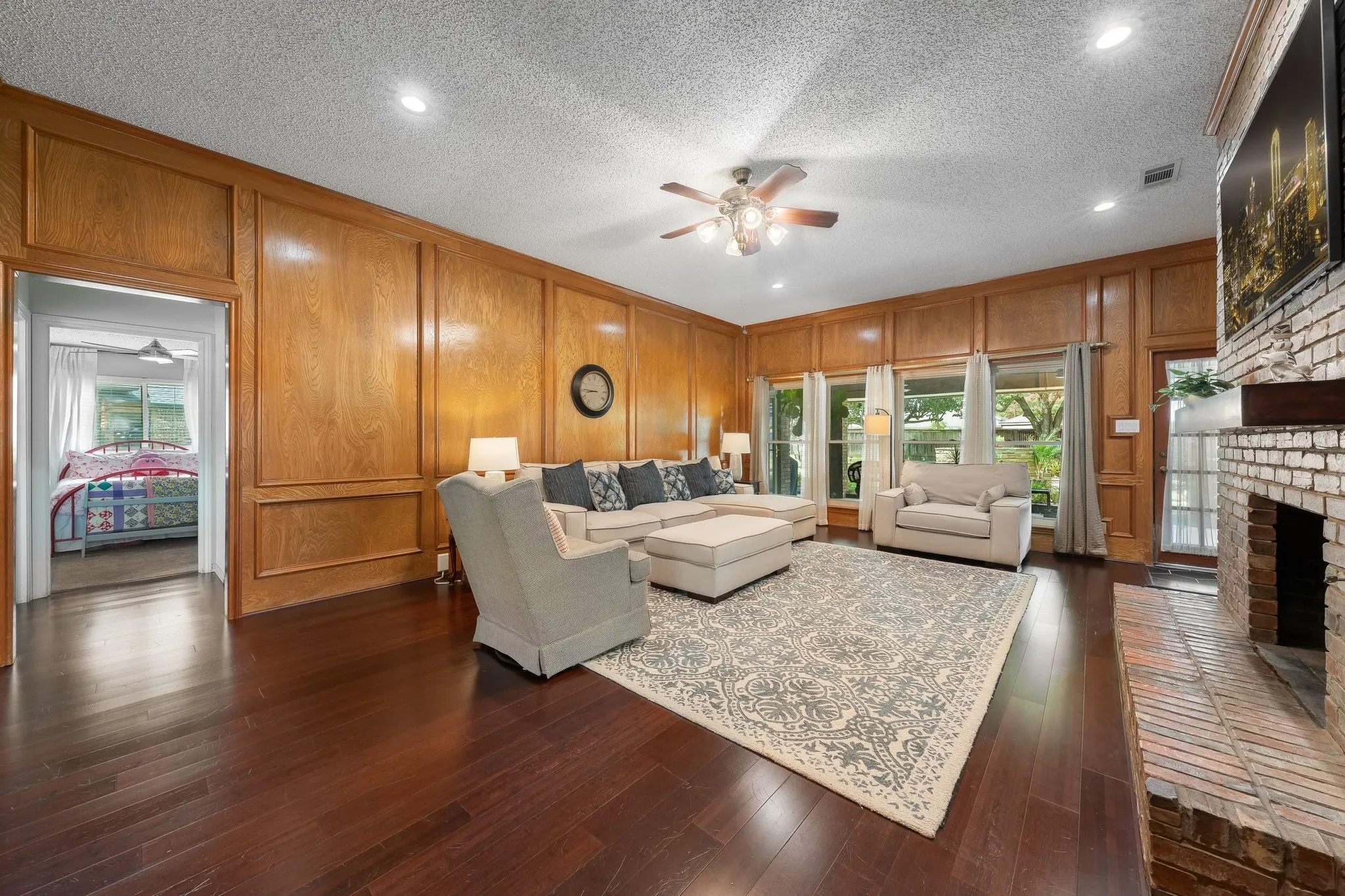 Spacious primary living area showcasing rich wood-finish flooring, coffered wood-paneled walls, and a ceiling fan with integrated lighting