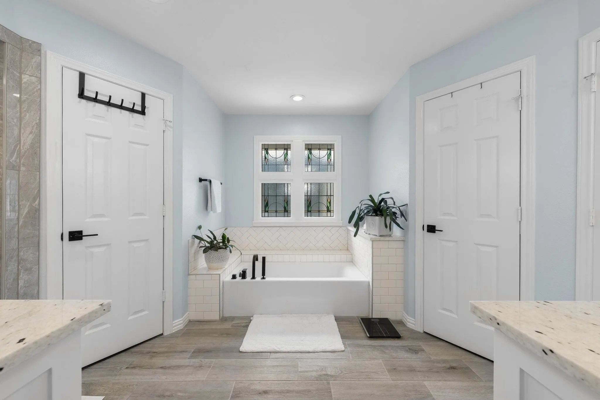 Deep soaking tub with subway tile surround, wood-finish flooring, and a decorative window