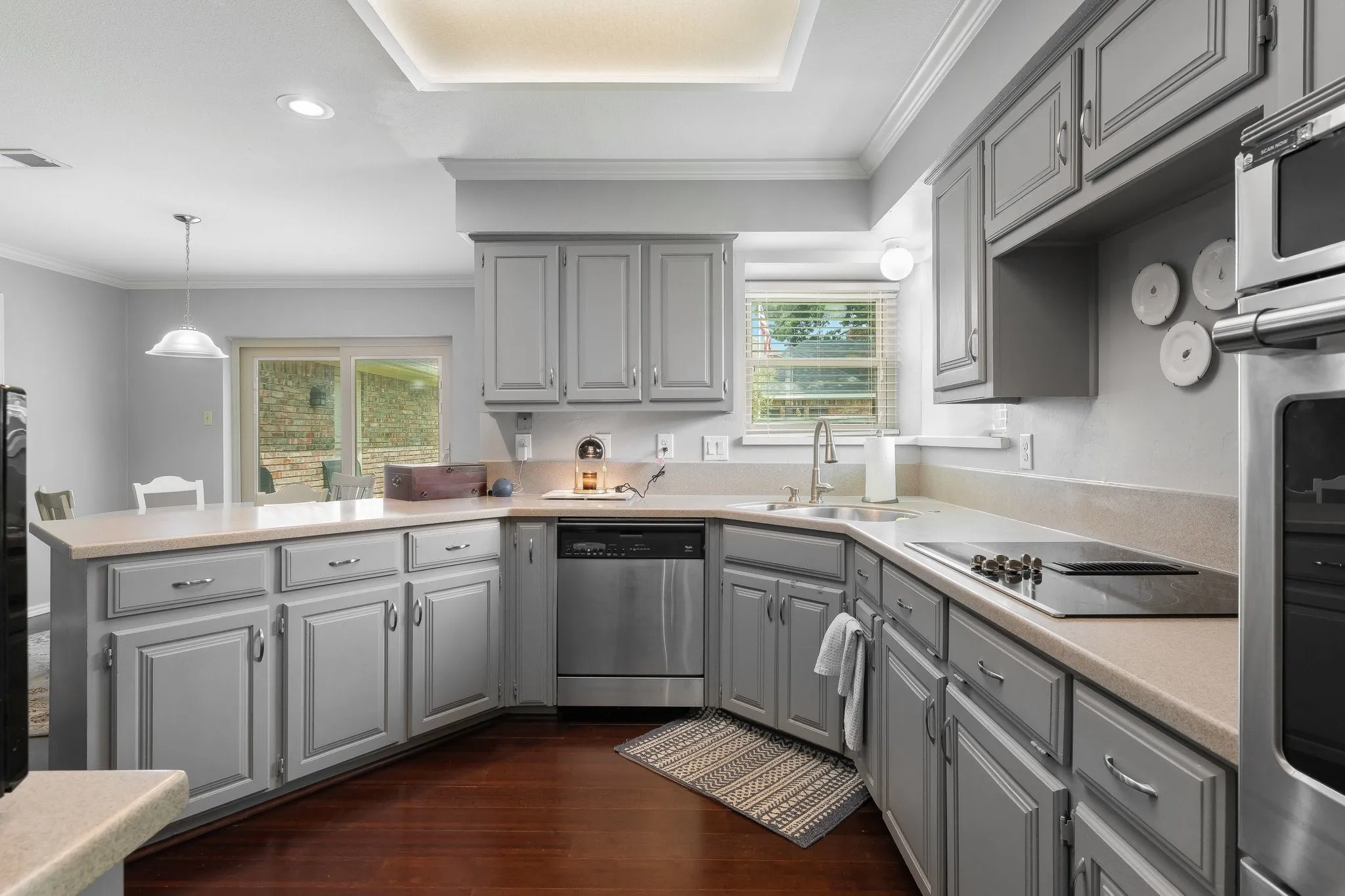 U-shaped kitchen featuring grey cabinetry, stainless steel appliances, a built-in cooktop, and light-toned countertops