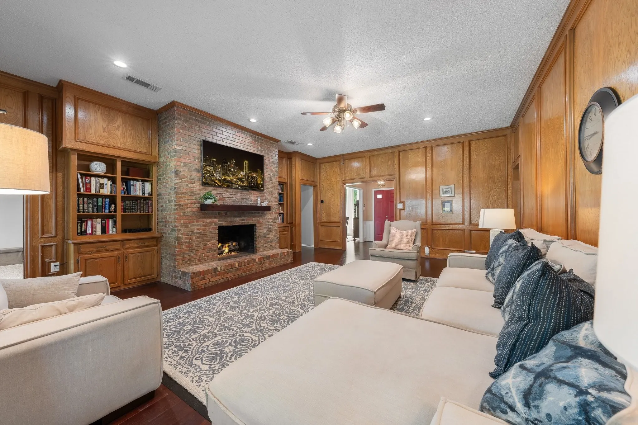 Brick fireplace with a wood mantel, built-in shelving, wood paneling, and wood-finish flooring