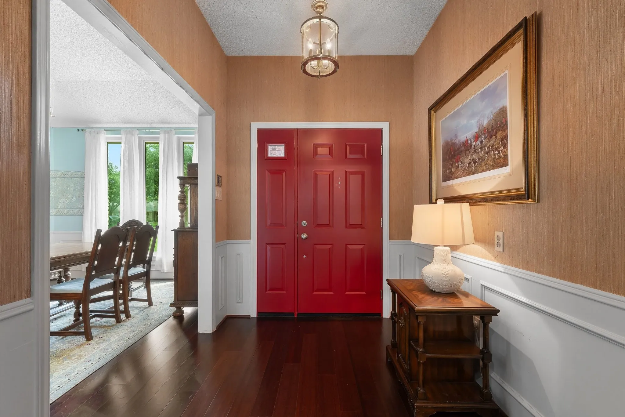 Brand New entry doors, dark wood-finish flooring, wainscoting, and a decorative ceiling fixture