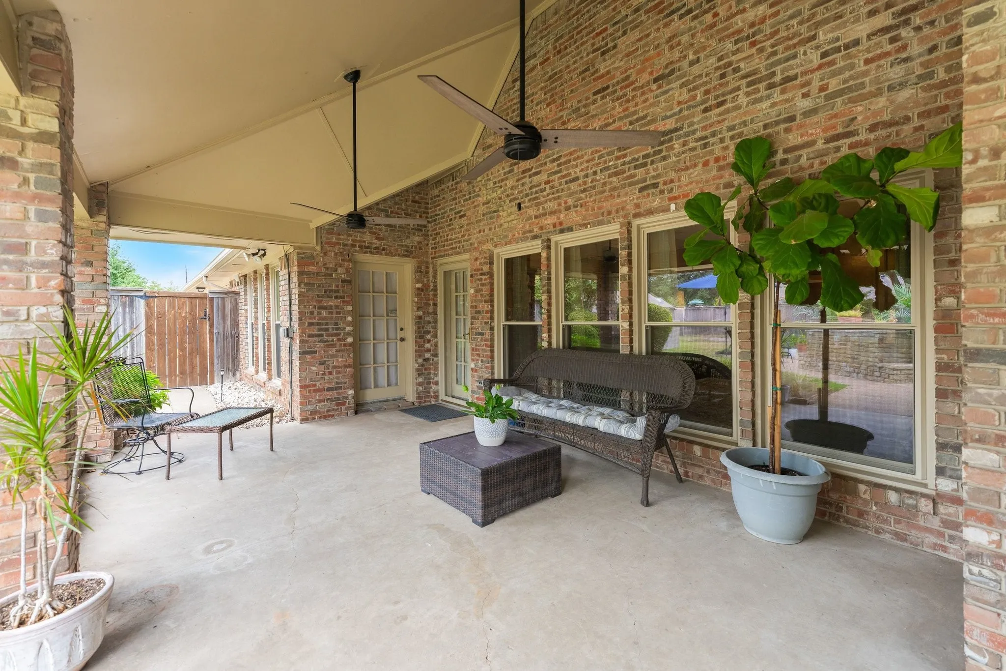 Expansive covered patio with a concrete surface, brick wall, and two ceiling fans
