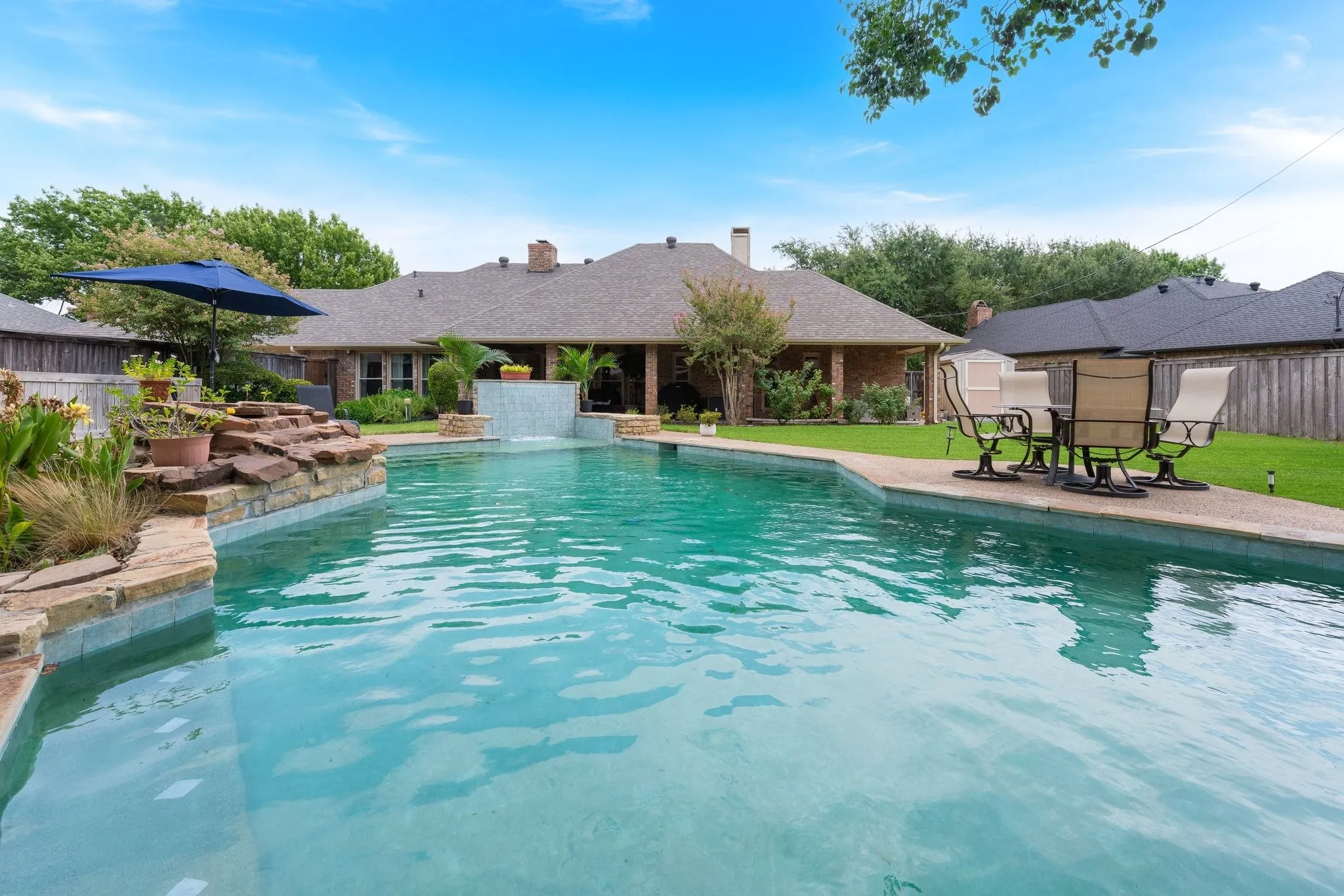 Expansive pool with a stone waterfall feature and integrated water wall, surrounded by a concrete patio and manicured lawn