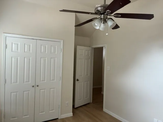 Vaulted ceiling, ceiling fan with integrated lighting, wood-finish flooring, paneled bifold closet doors, and a paneled interior door