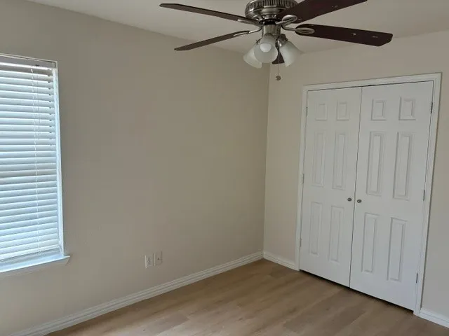 Wood-finish flooring with white trim, a ceiling fan with integrated lighting, and a window with blinds