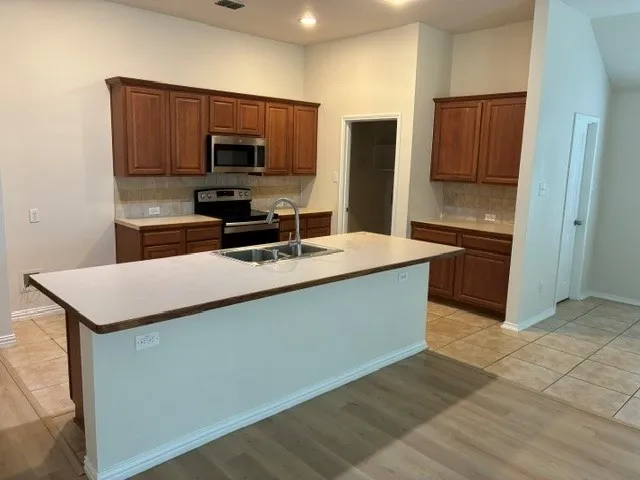 Kitchen featuring wood-finish cabinetry, stainless steel appliances, a center island with sink, tile backsplash, and recessed lighting